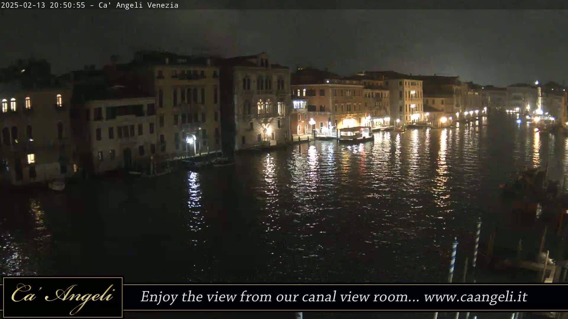 A nighttime view of a canal in Venice, with buildings lining both sides, reflecting lights on the dark water.