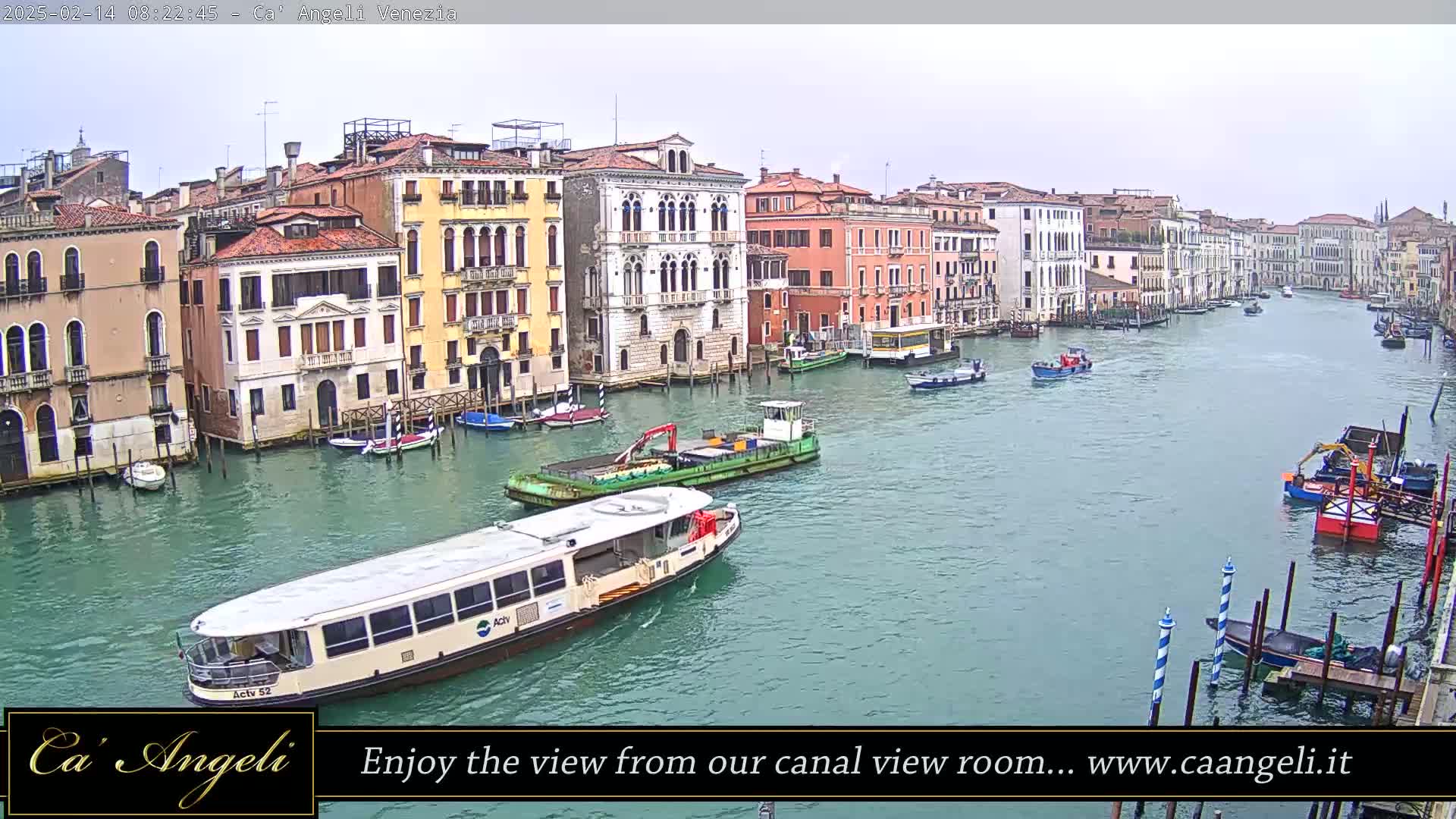 A waterway in Venice, Italy, is shown on an overcast day, with numerous buildings lining the canal and several boats, including a passenger ferry, traversing the water.