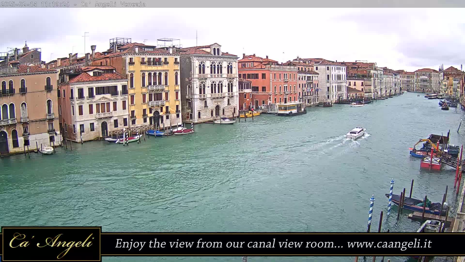 A wide shot of a canal in Venice, Italy, on an overcast day, shows several buildings lining the waterway with boats moored along the sides and a few moving in the water.
