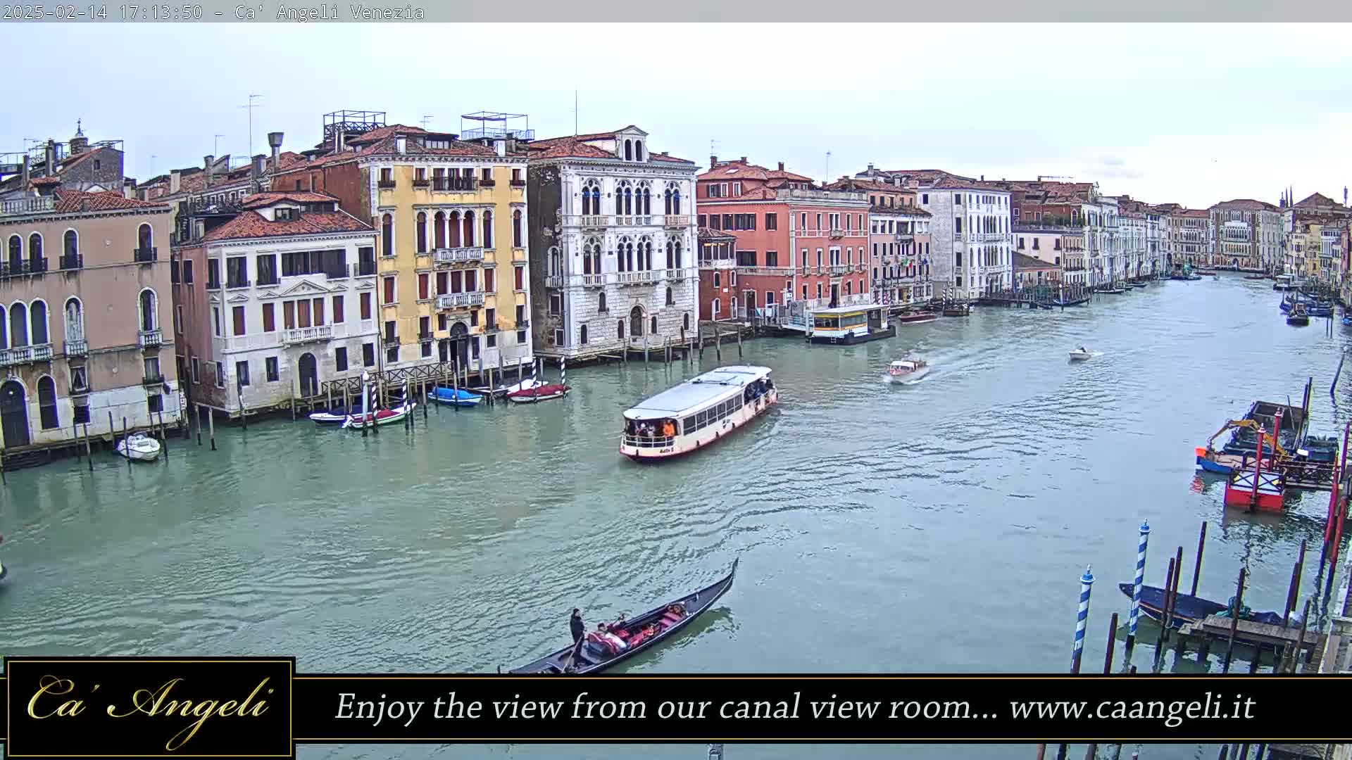 A wide shot shows a waterway in Venice with several buildings lining the canal, various boats, including a gondola and a water bus, and an overcast sky.