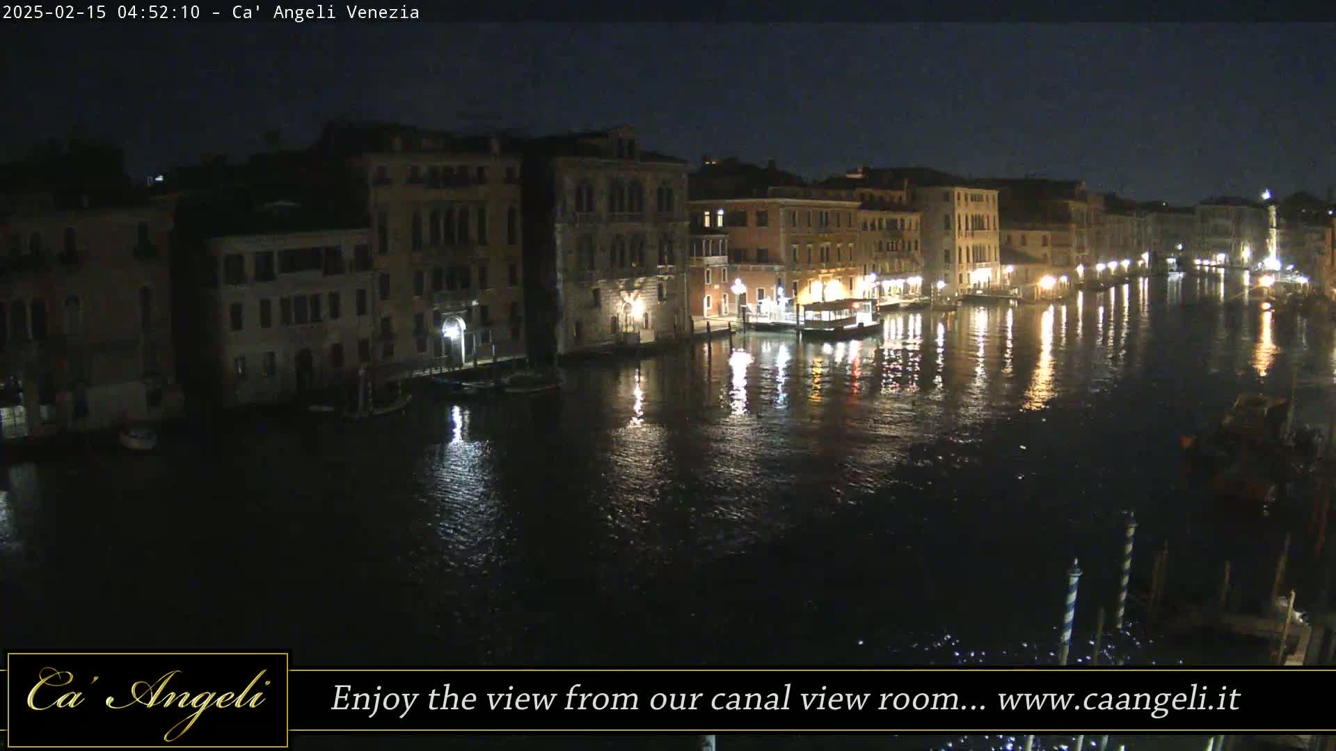 A nighttime view of a canal in Venice, Italy, shows several buildings illuminated along the waterway, with their lights reflecting on the dark water.
