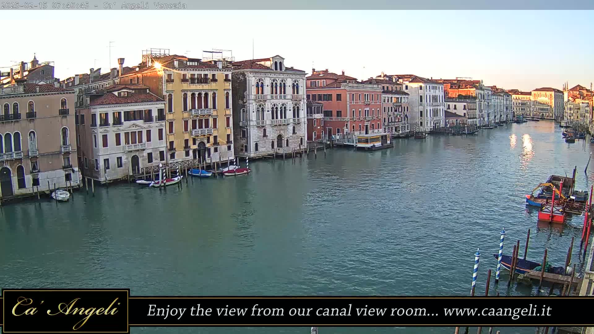 A calm canal in Venice, Italy, reflects the sunrise light on its surface as boats are moored along the buildings lining its banks.