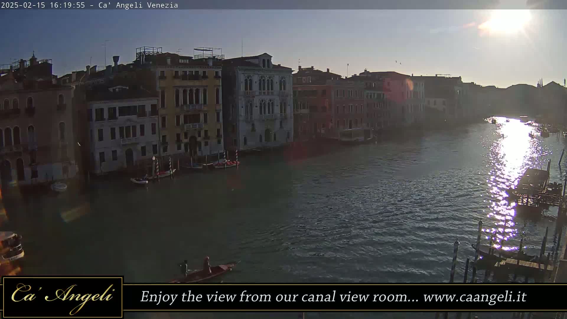A gondola floats on a sunlit canal in Venice, alongside several buildings lining the waterway.