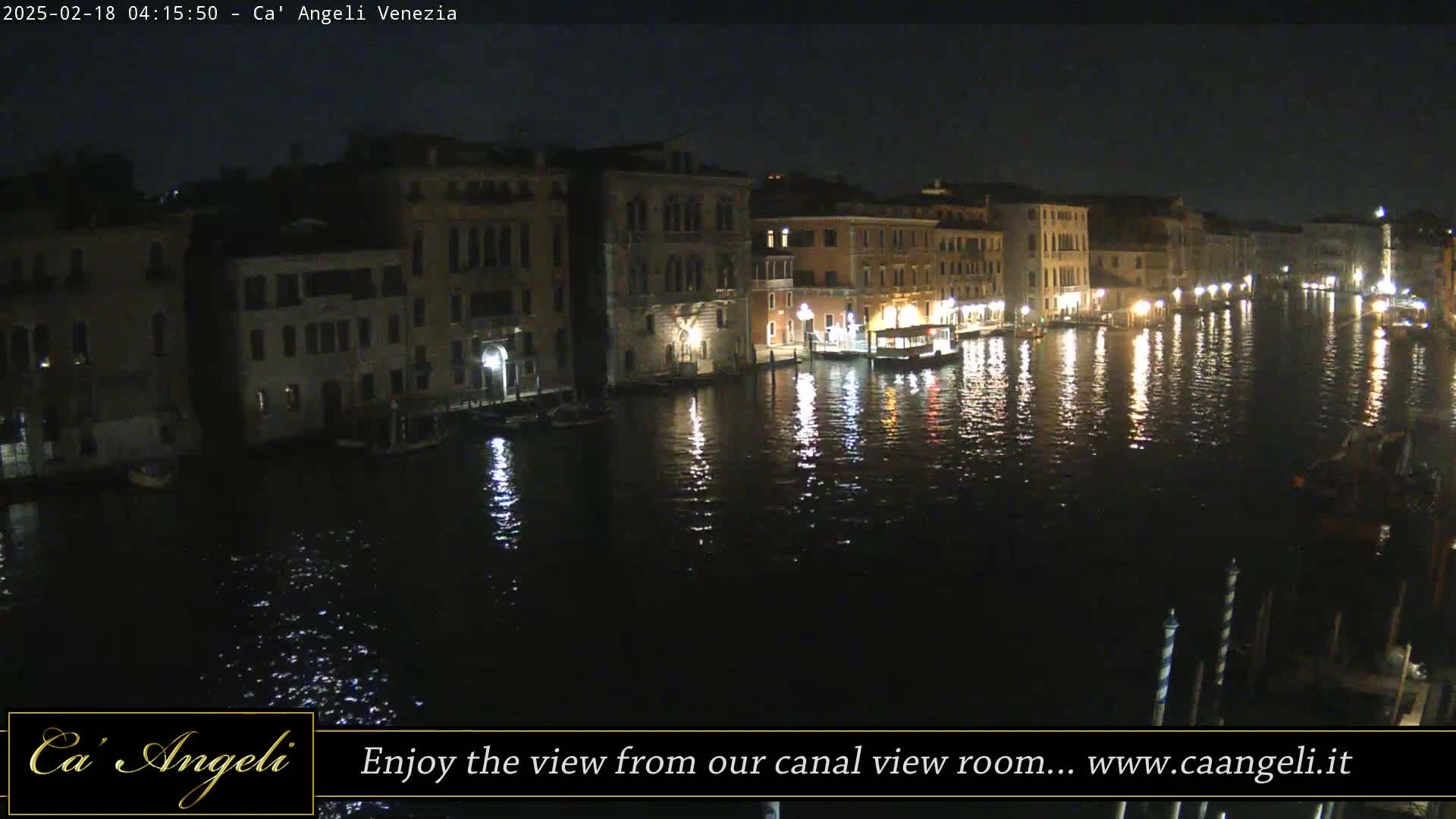 At night, illuminated buildings line a calm canal reflecting lights on its dark water.