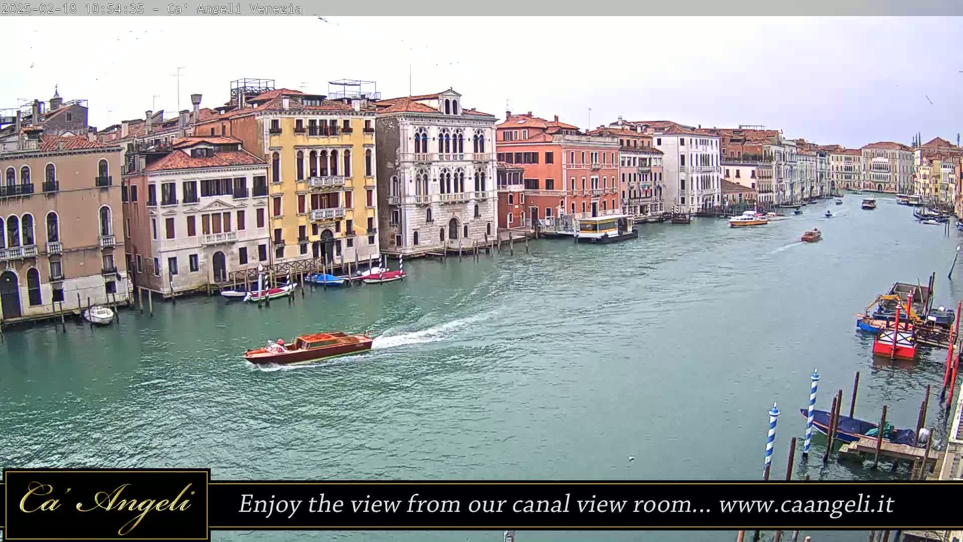 A waterway lined with multi-storied buildings is shown on an overcast day with several boats traveling along it.