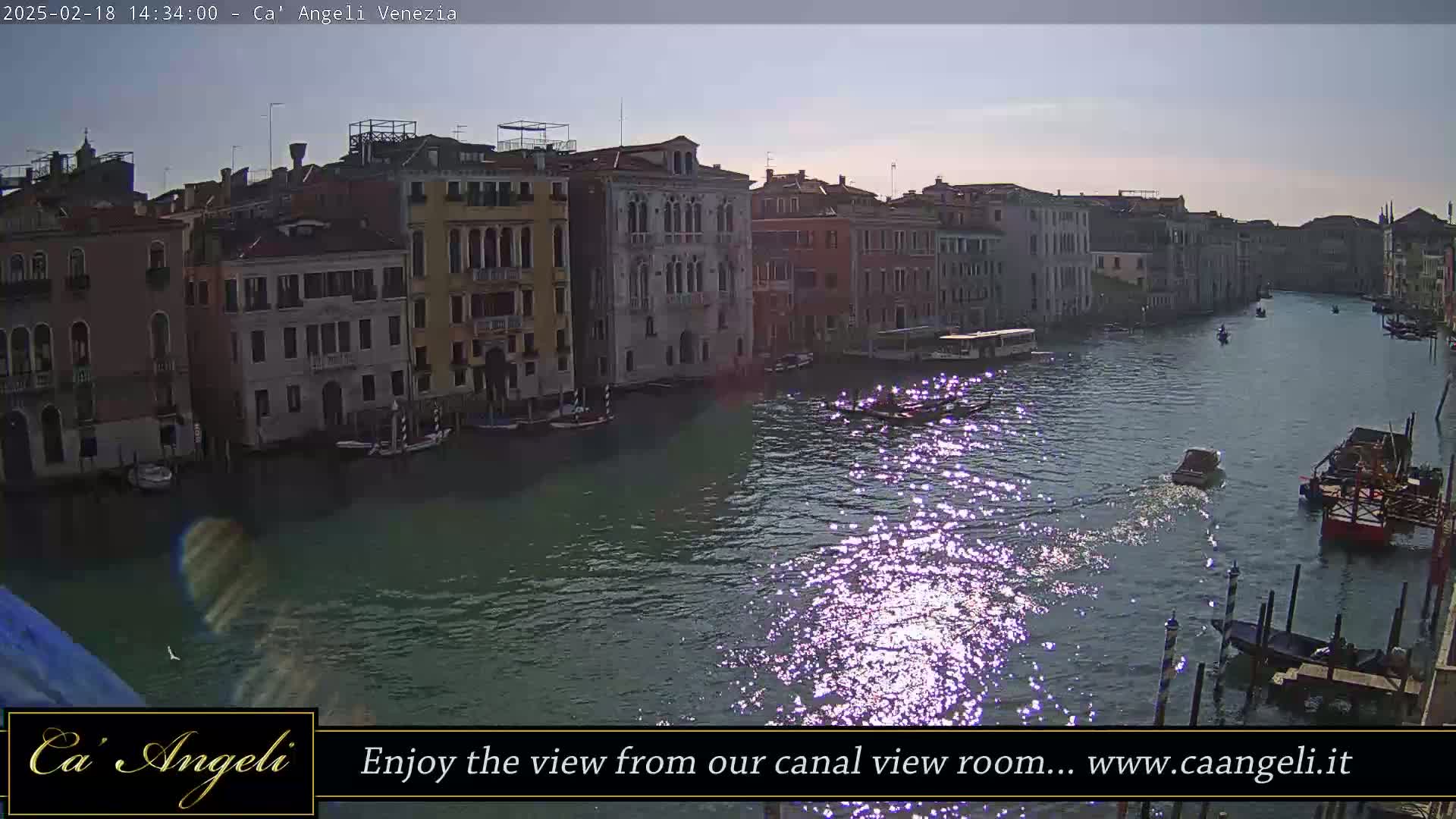 A sunny day in Venice shows a canal with several boats, reflecting sunlight, and lined with tall, narrow buildings.