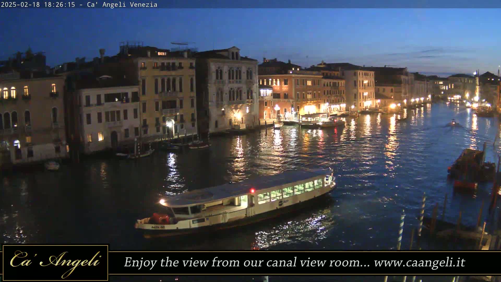 A waterway at twilight, lined with illuminated buildings, with several boats traversing the water.