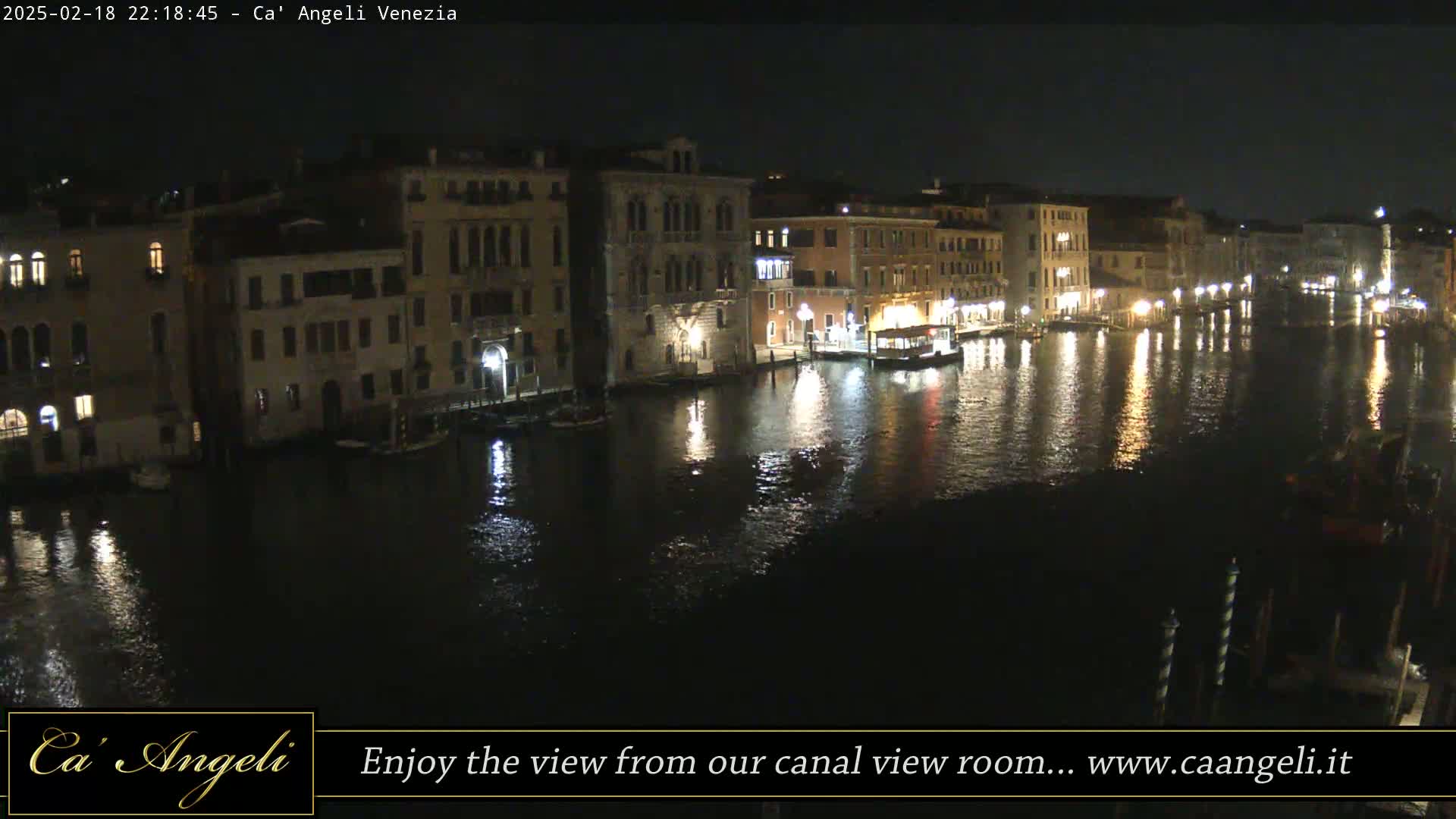 A nighttime view of a canal in Venice, with illuminated buildings lining the waterway and their lights reflecting on the dark water.