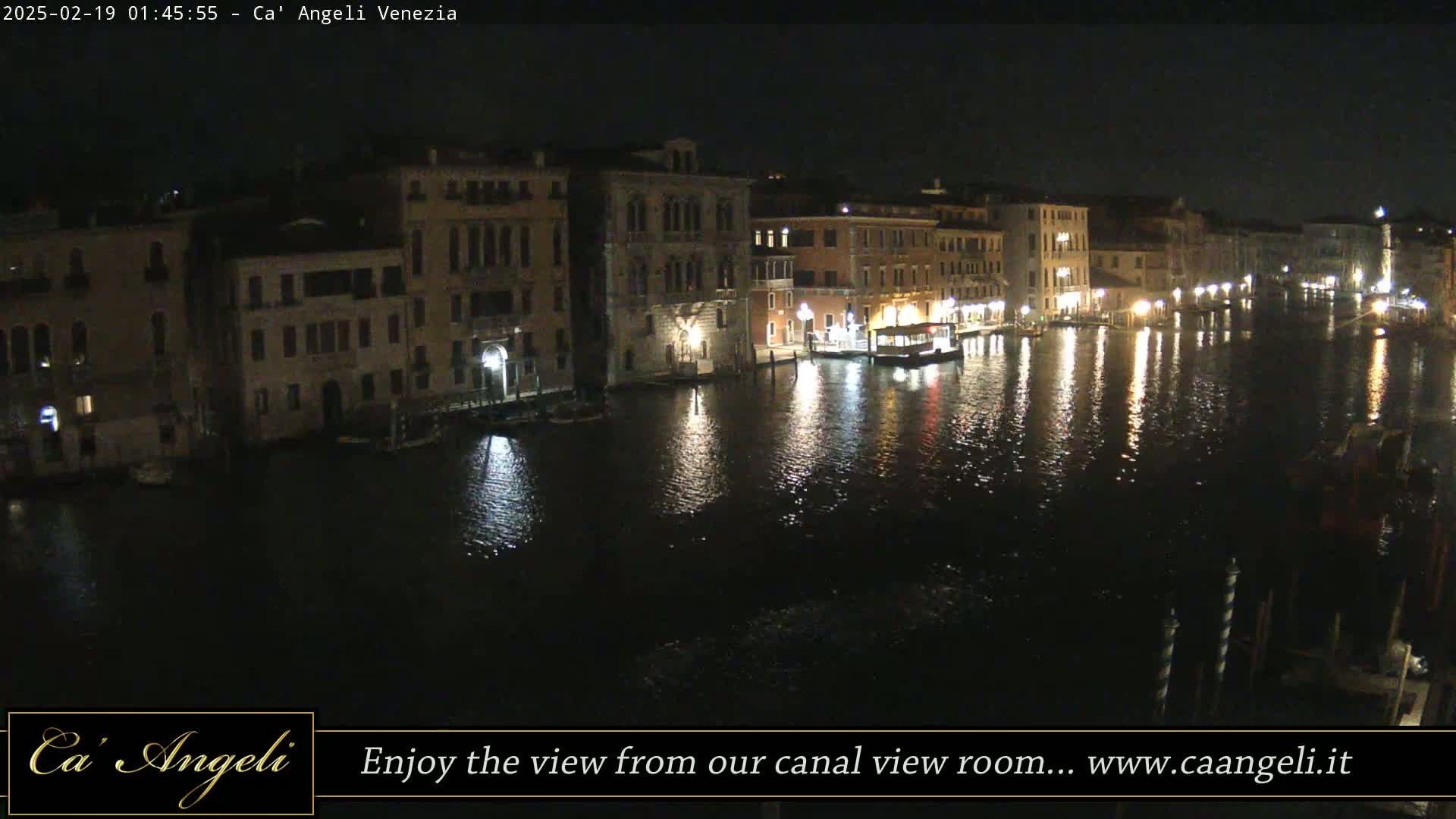A nighttime view of a canal in Venice, Italy, with illuminated buildings lining the waterway and their lights reflecting on the dark water.