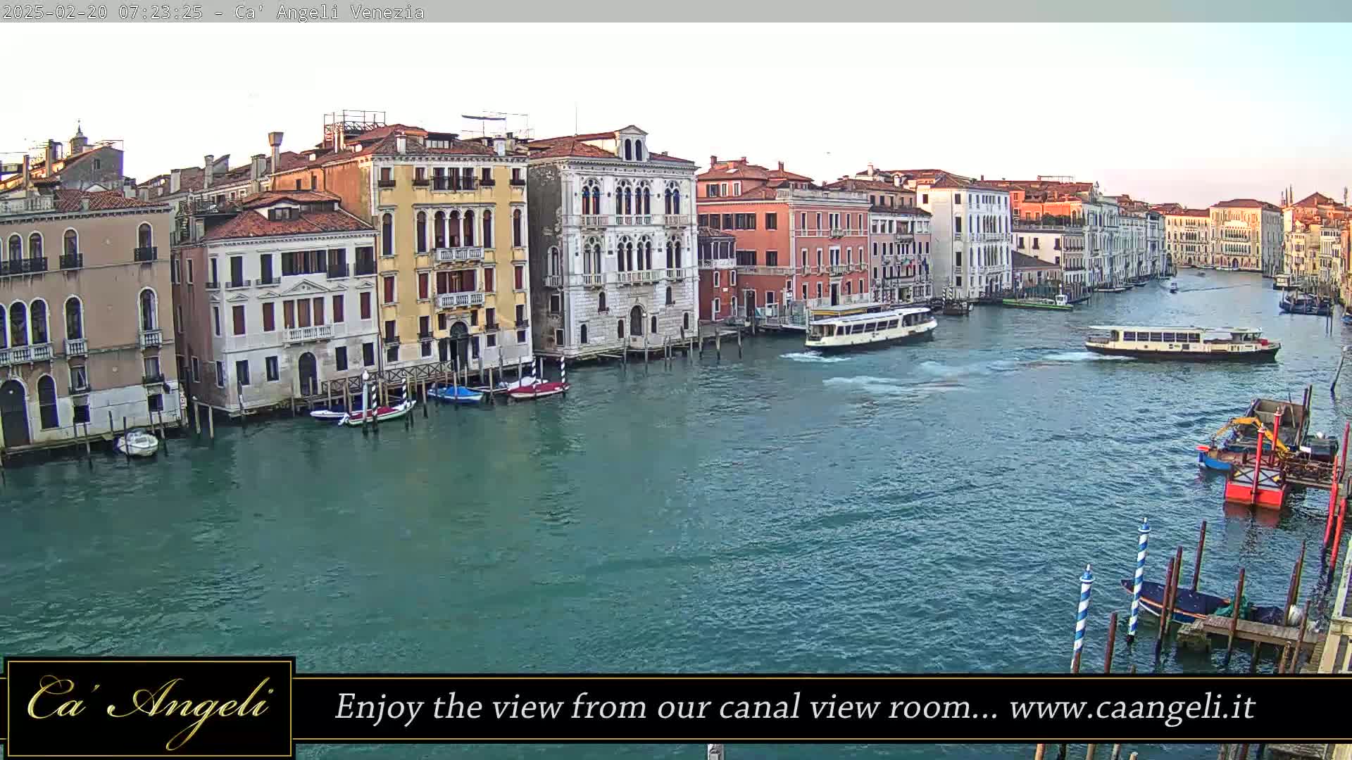 A wide shot of a waterway in Venice, Italy, shows several buildings lining the canal, with boats and water traffic visible under a partly cloudy sky.