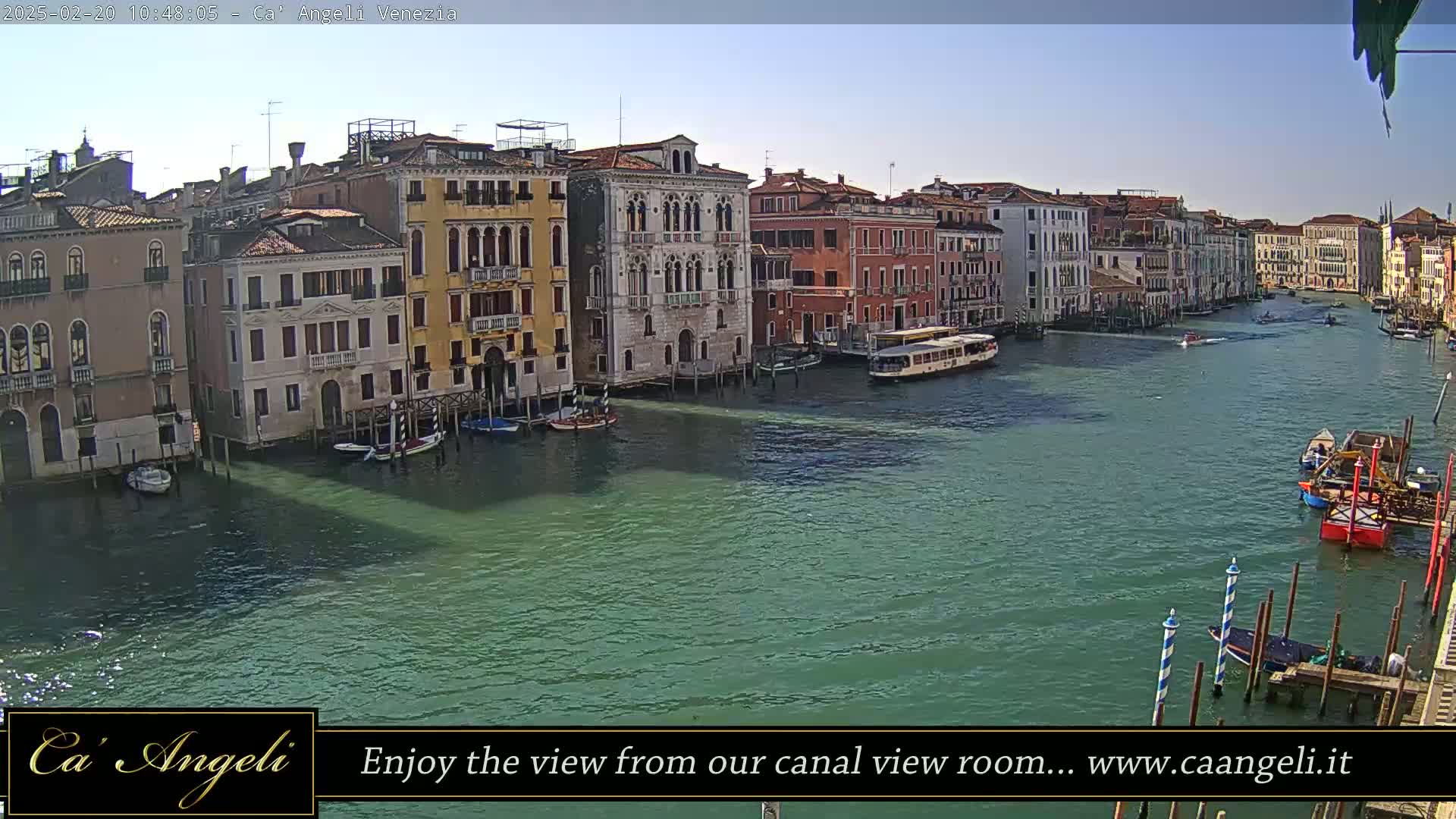 A sunny day in Venice shows a wide canal with several boats and buildings lining the waterway.