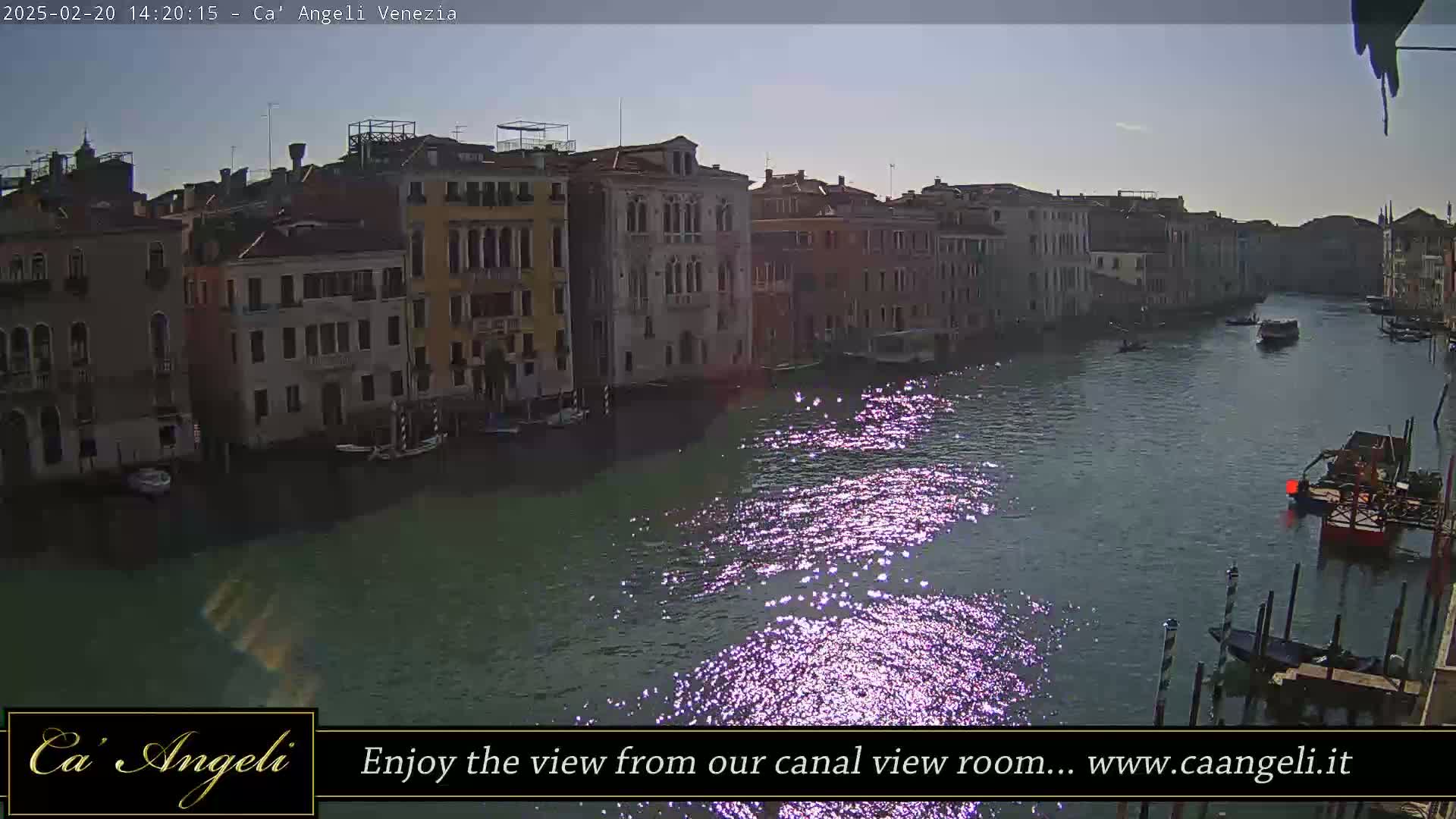 A sunny day reveals a Venetian canal reflecting sunlight, with several boats and buildings lining its banks.