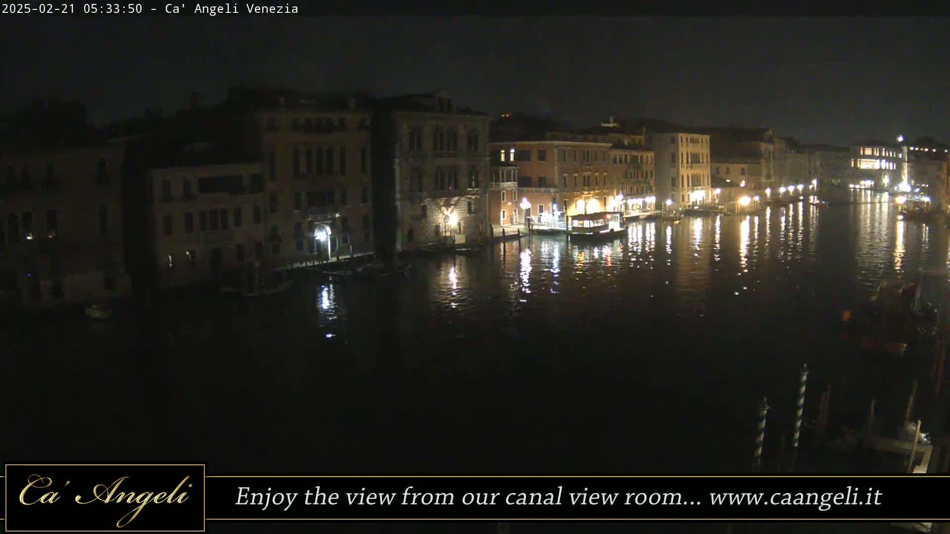 At night, a canal in Venice is illuminated by lights reflecting on the dark water, with buildings lining both sides.