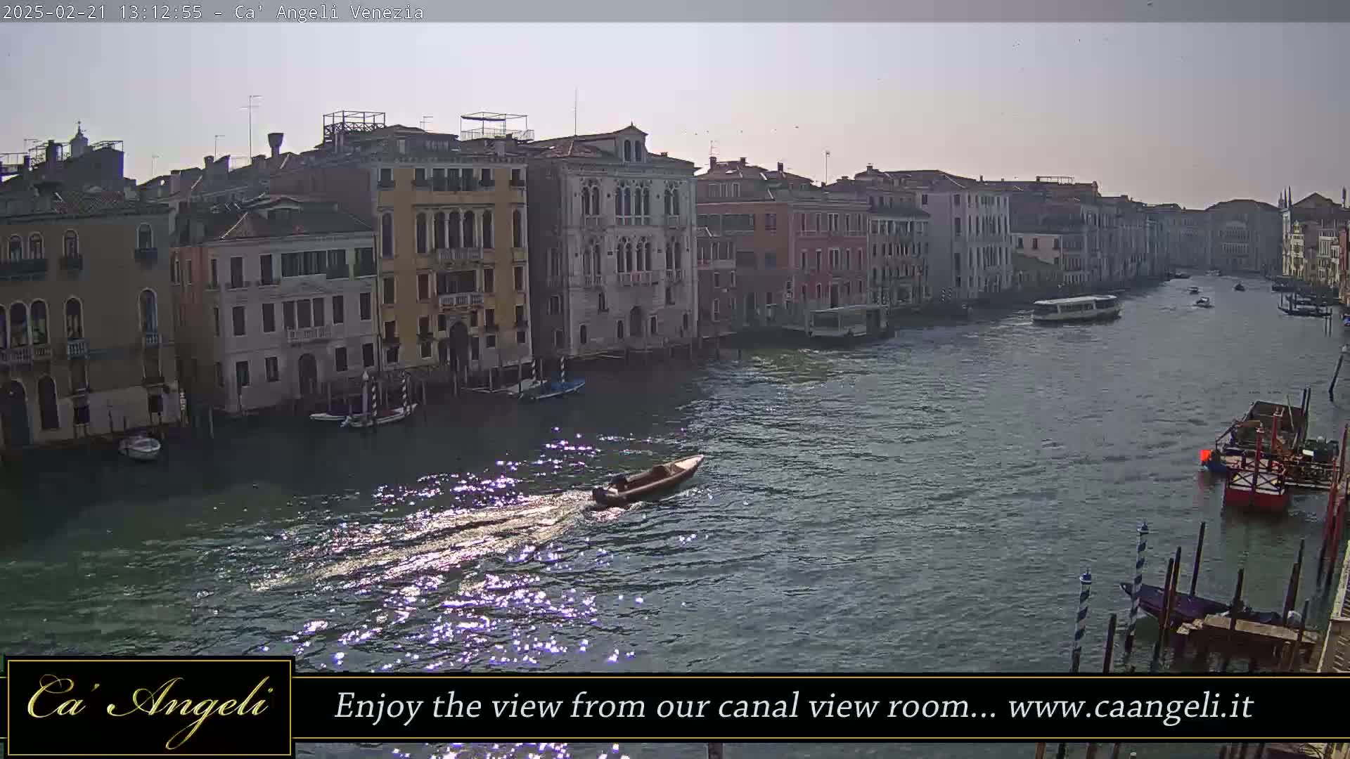 A sunny day shows a canal in Venice with several boats and buildings lining the waterway.