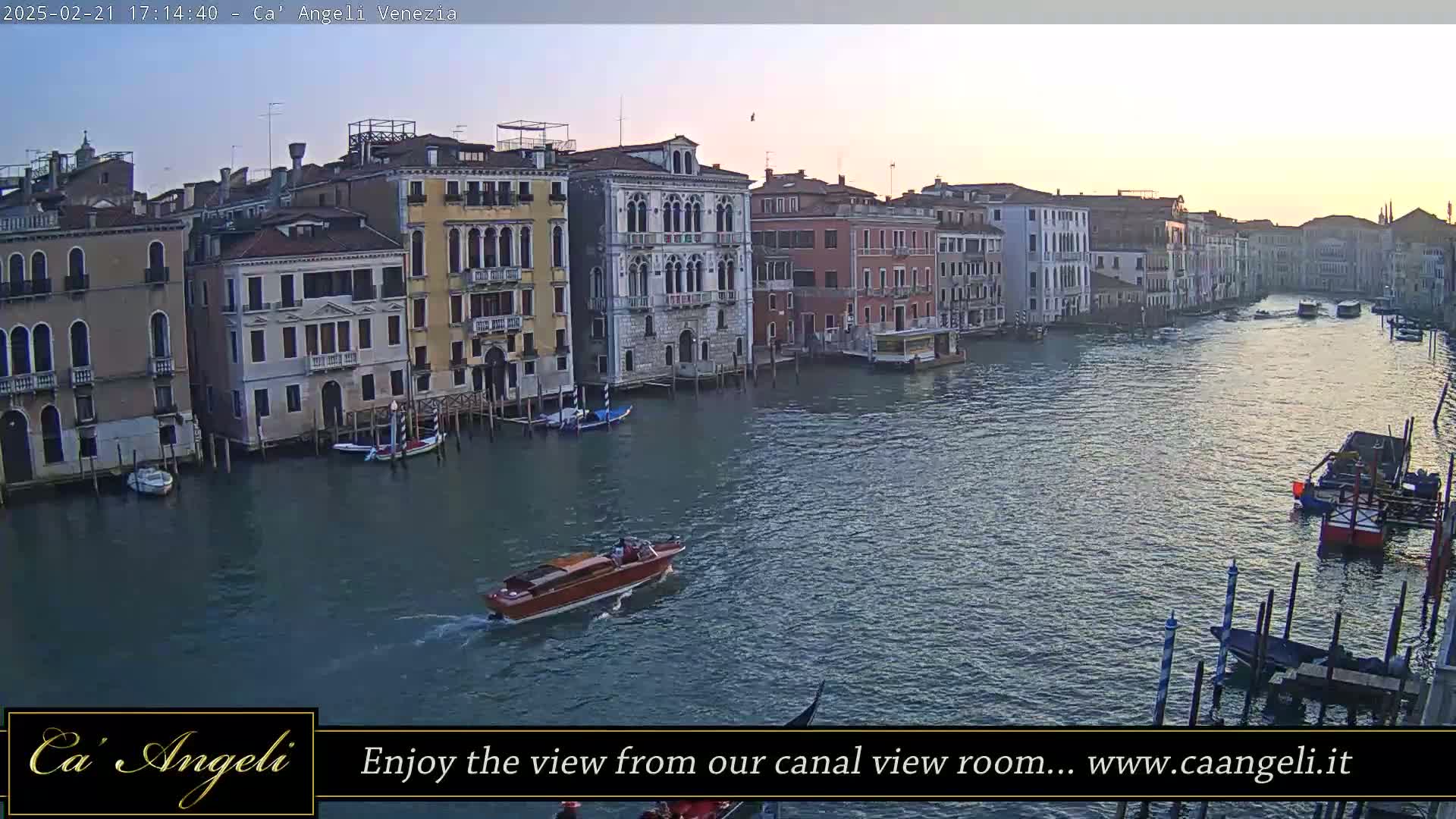 A calm canal in Venice, Italy, is lined with tall buildings at sunset, with several boats moving along the waterway.