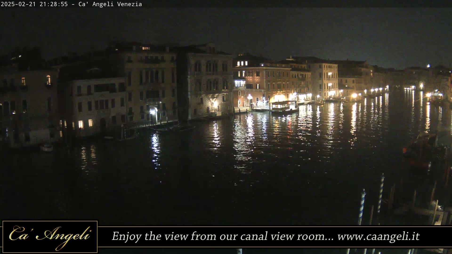 A nighttime view of a canal in Venice, with illuminated buildings lining the waterway and their reflections shimmering on the water's surface.