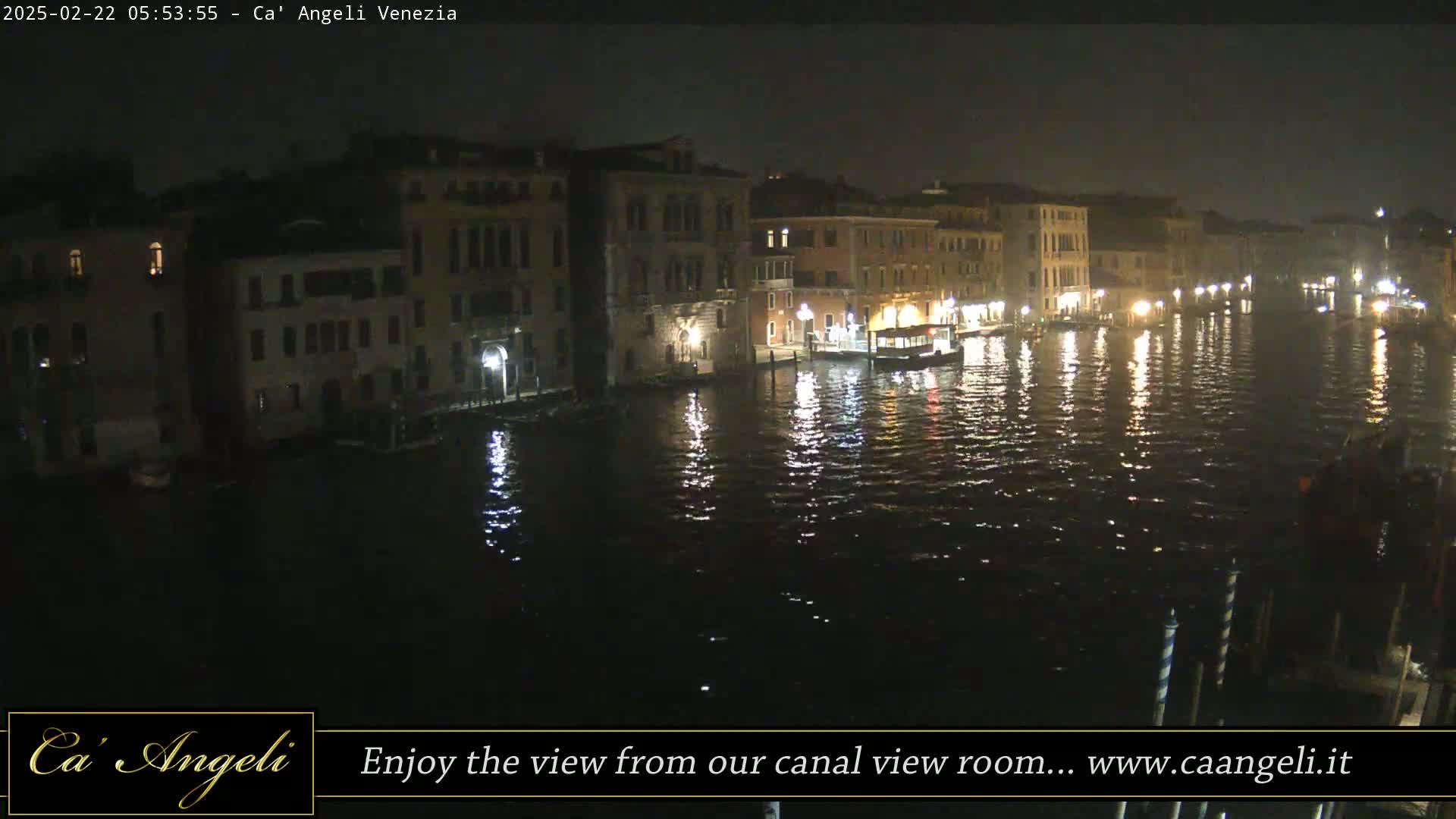A nighttime view of a canal in Venice, with illuminated buildings lining the waterway and a boat on the water.