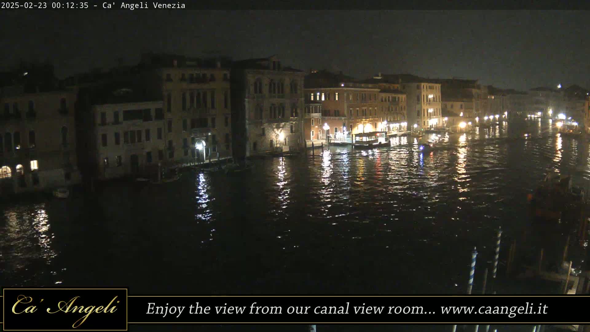 A nighttime view of a canal in Venice, showing several buildings along the waterway reflecting lights onto the dark water.