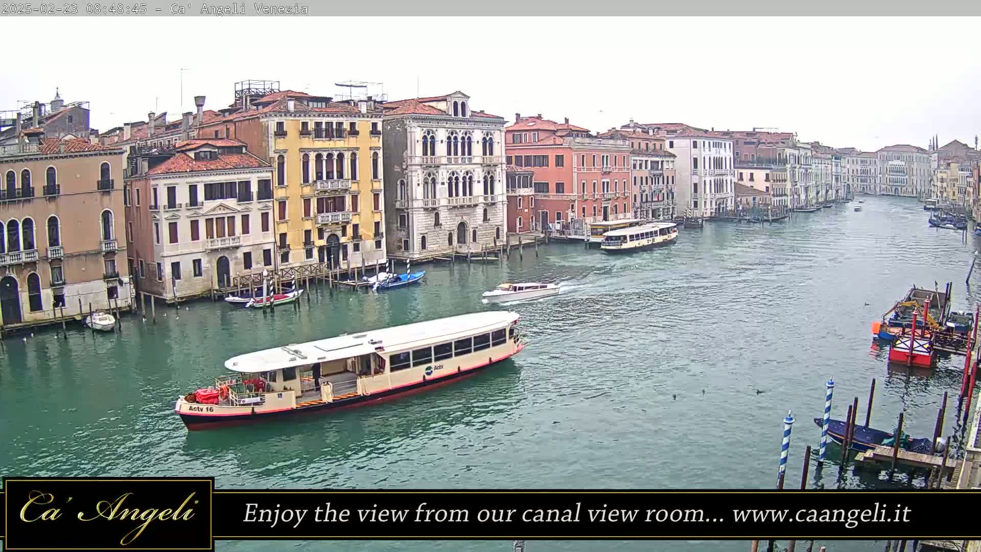 A wide shot of a Venetian canal shows several boats, including a water bus, passing colorful buildings under an overcast sky.