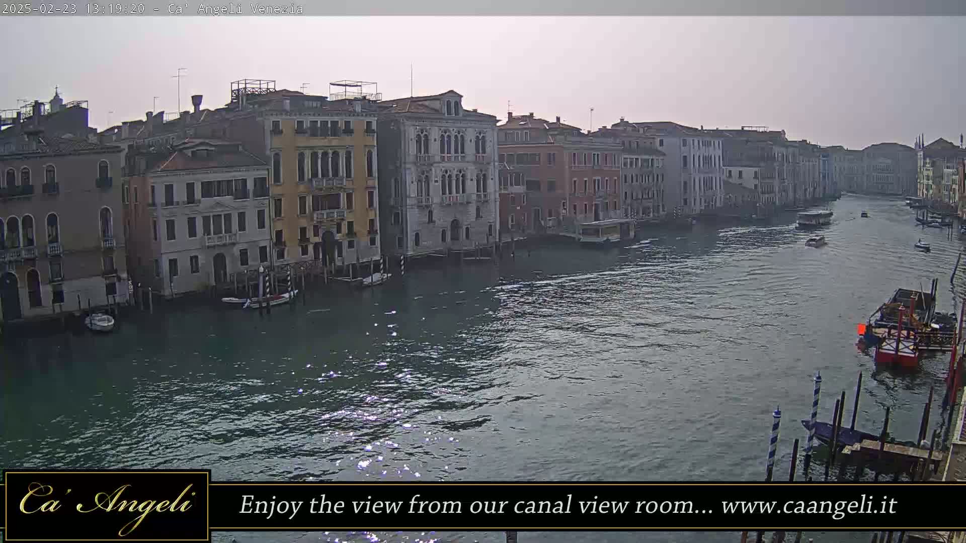 A wide shot of a calm canal in Venice, lined with several multi-story buildings under an overcast sky.