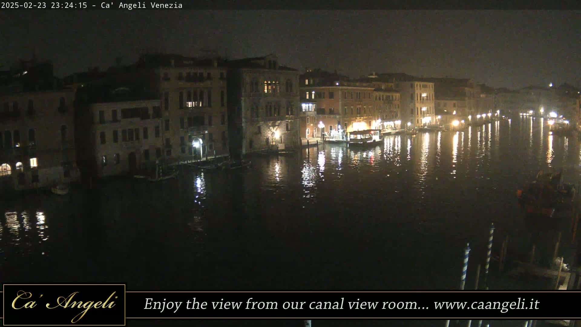 A nighttime view of a canal in Venice, with buildings lining the waterway and their lights reflected in the dark water.