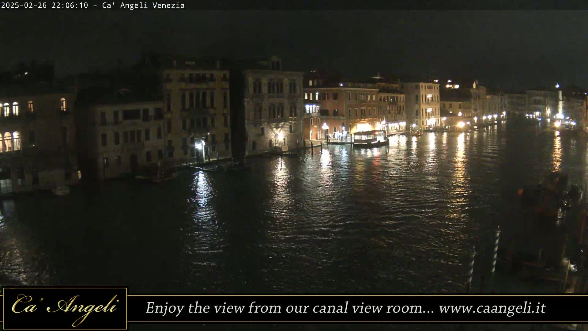 A nighttime view of a canal in Venice, with illuminated buildings lining its banks and boats moored along the waterway.