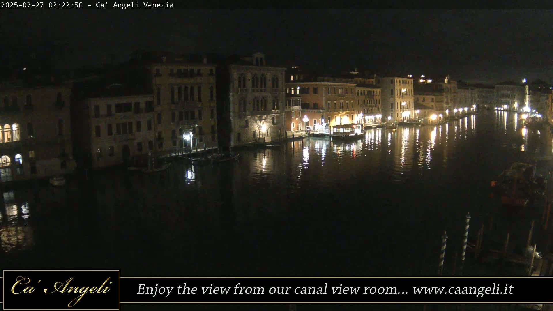 A nighttime view of a canal in Venice, lined with illuminated buildings, reflecting in the dark water.