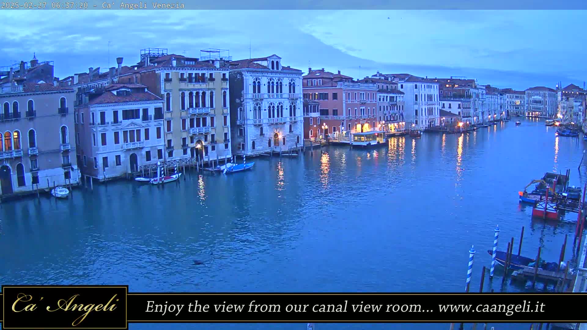 Under a twilight sky, numerous buildings line a canal, with boats moored along its banks.