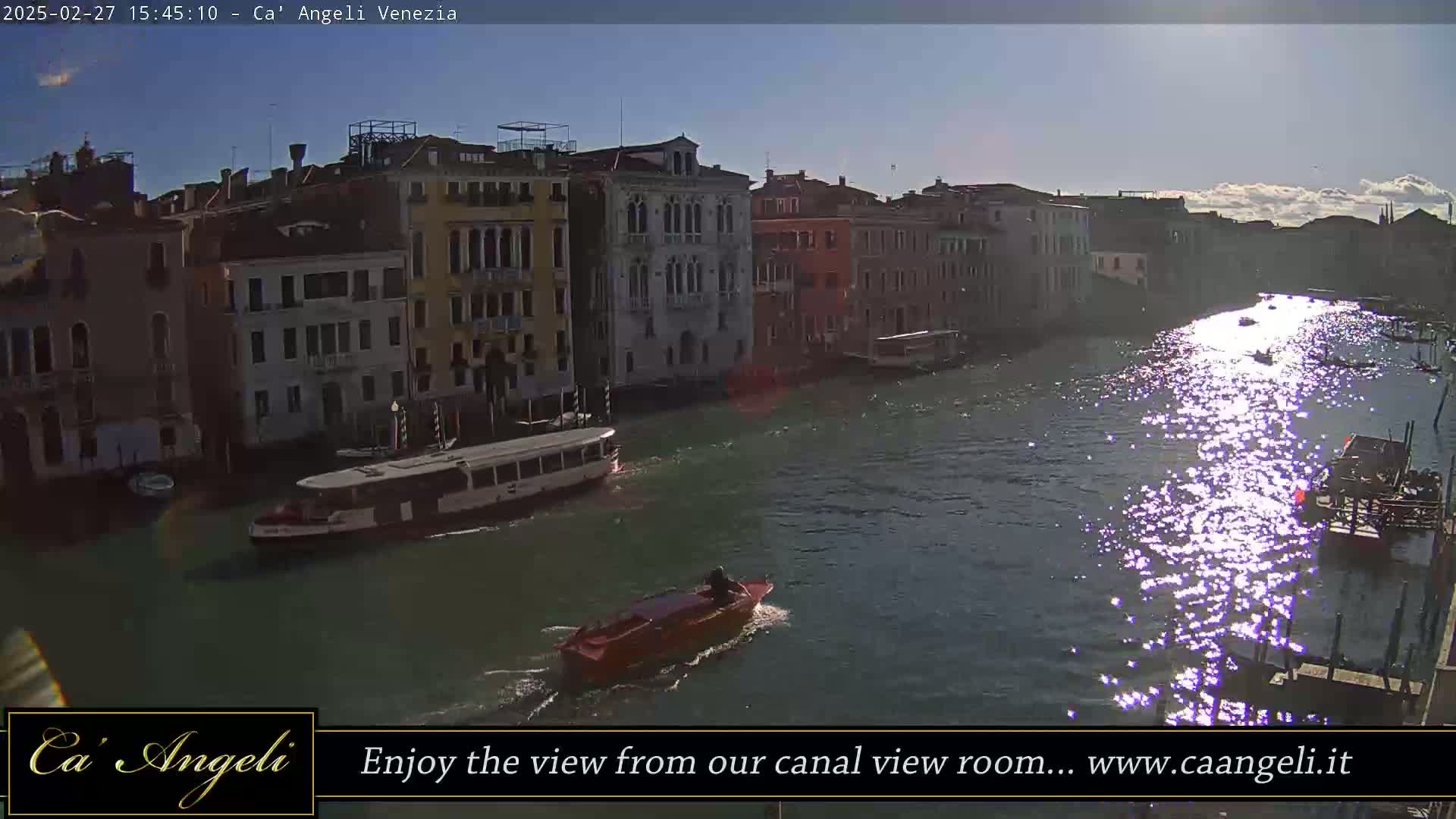 A sunny day in Venice shows a canal with several boats, including a larger passenger ferry, and buildings lining the waterway.