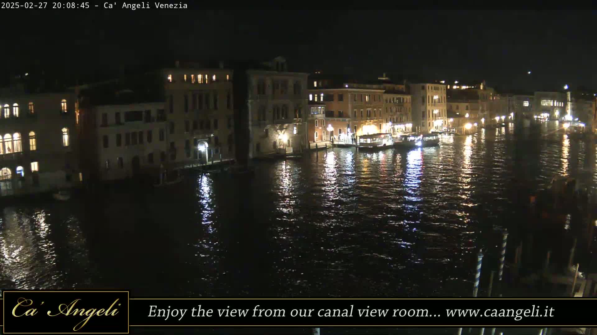 A nighttime view of a canal in Venice, with buildings lining the waterway, their lights reflecting on the dark water.