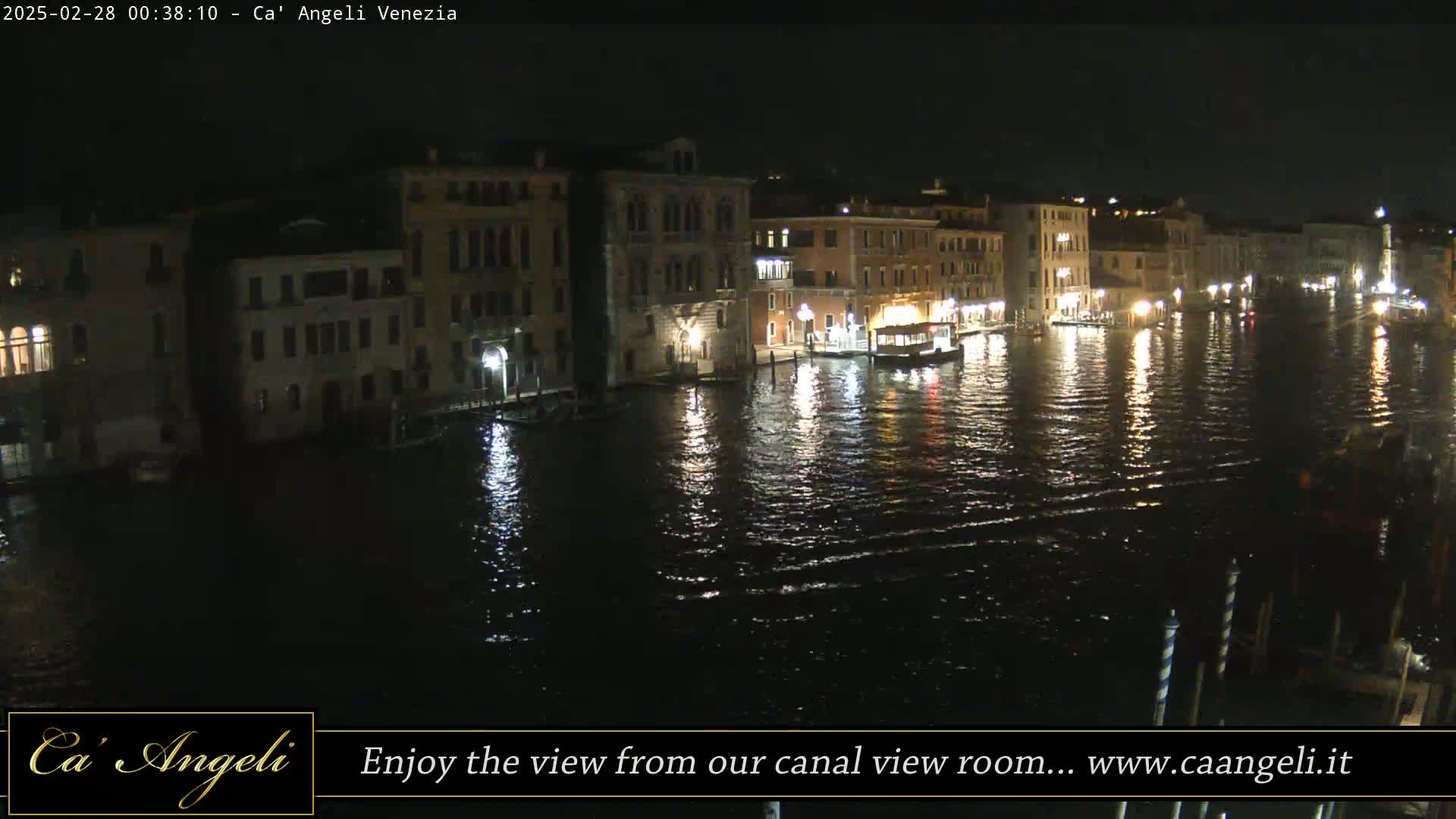 A nighttime view of a canal in Venice, Italy, with illuminated buildings lining the waterway and boats on the water.