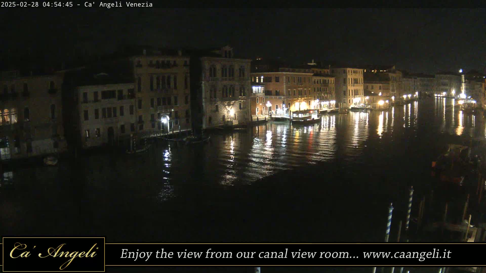 A nighttime view of a canal in Venice, with buildings illuminated along the waterway and their reflections visible in the dark water.