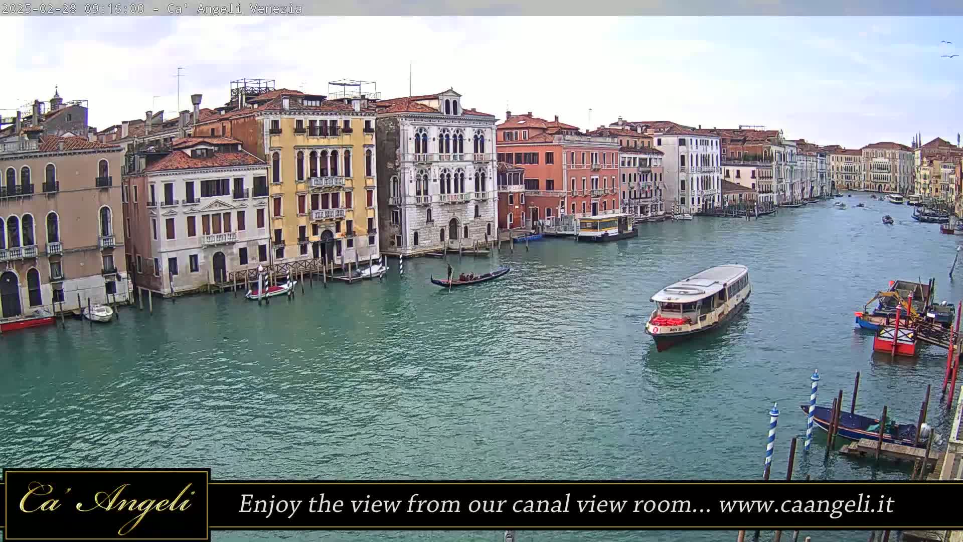A wide shot of a canal in Venice, Italy, under a cloudy sky, shows numerous buildings lining the waterway with gondolas and water taxis on the water.