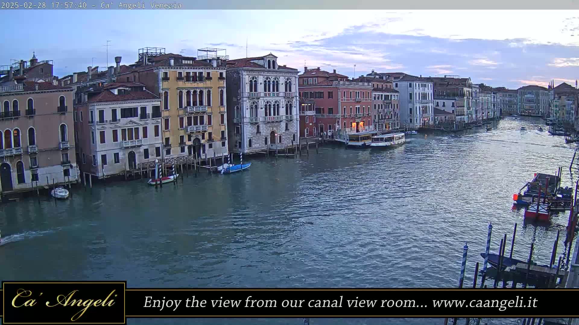A wide shot of a Venetian canal at dusk shows numerous buildings lining the waterway, with boats and water traffic visible on the water.