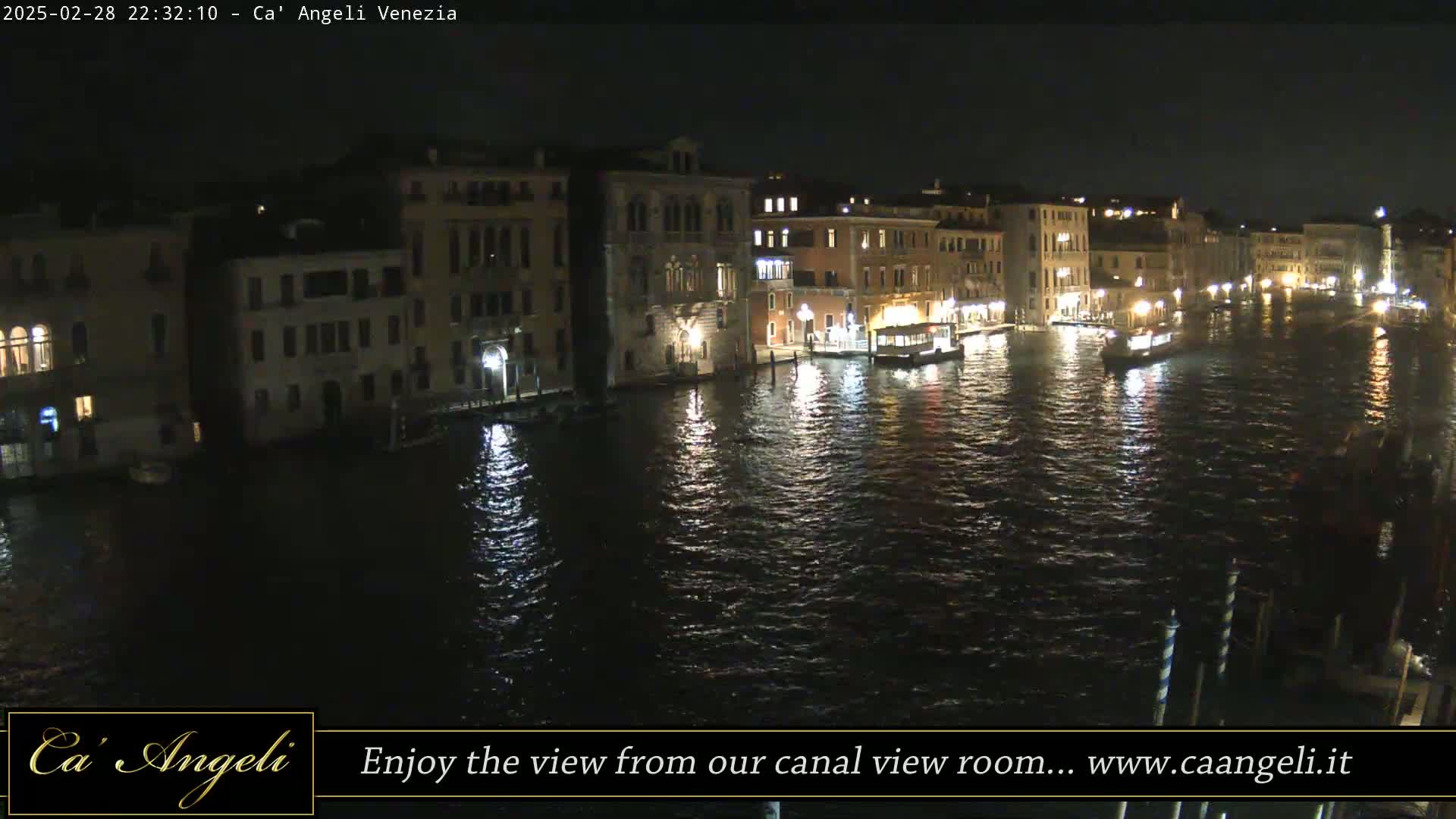 A nighttime view of a canal in Venice, showing illuminated buildings and boats on the water.