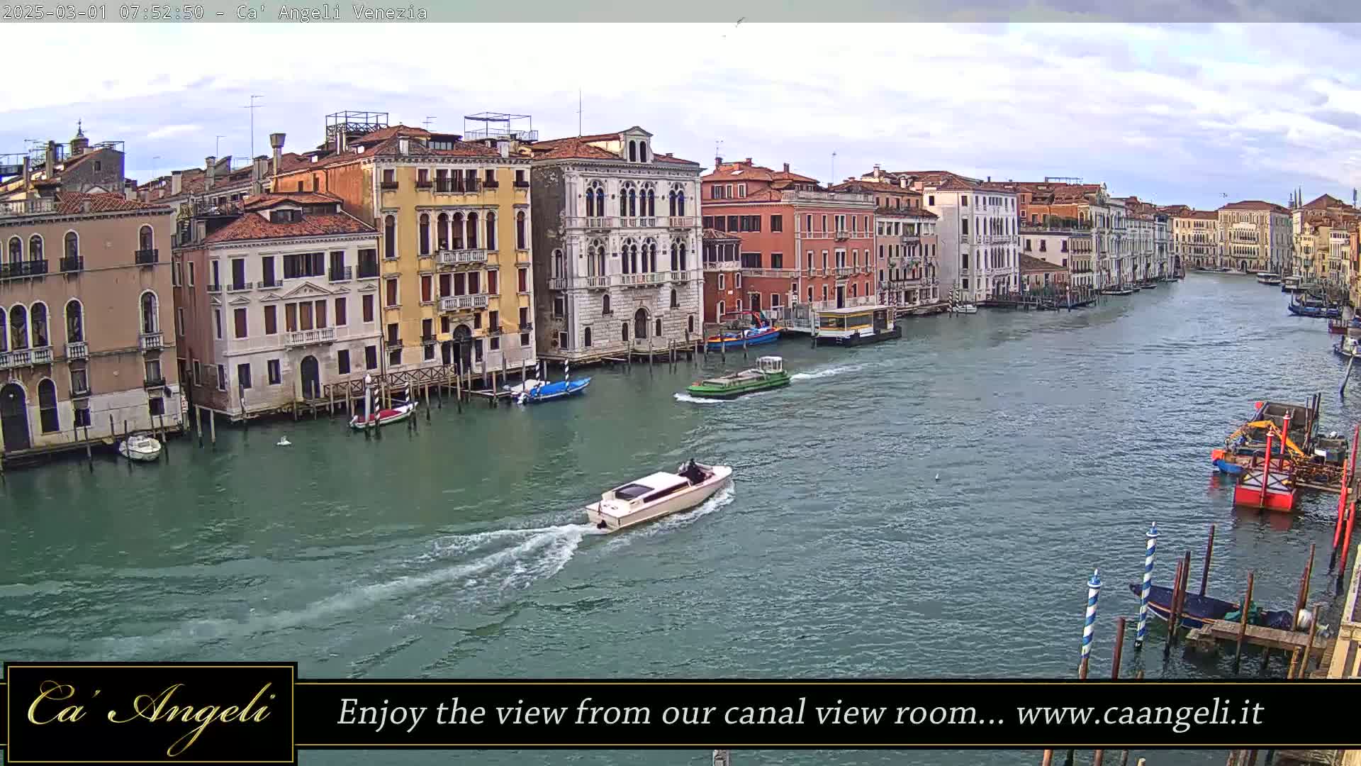 A canal in Venice, under a cloudy sky, shows several boats and colorful buildings lining its banks.