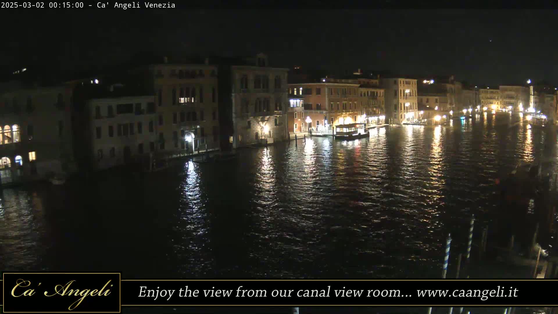 A nighttime view of a canal in Venice, showing illuminated buildings along the waterway and a boat on the water.