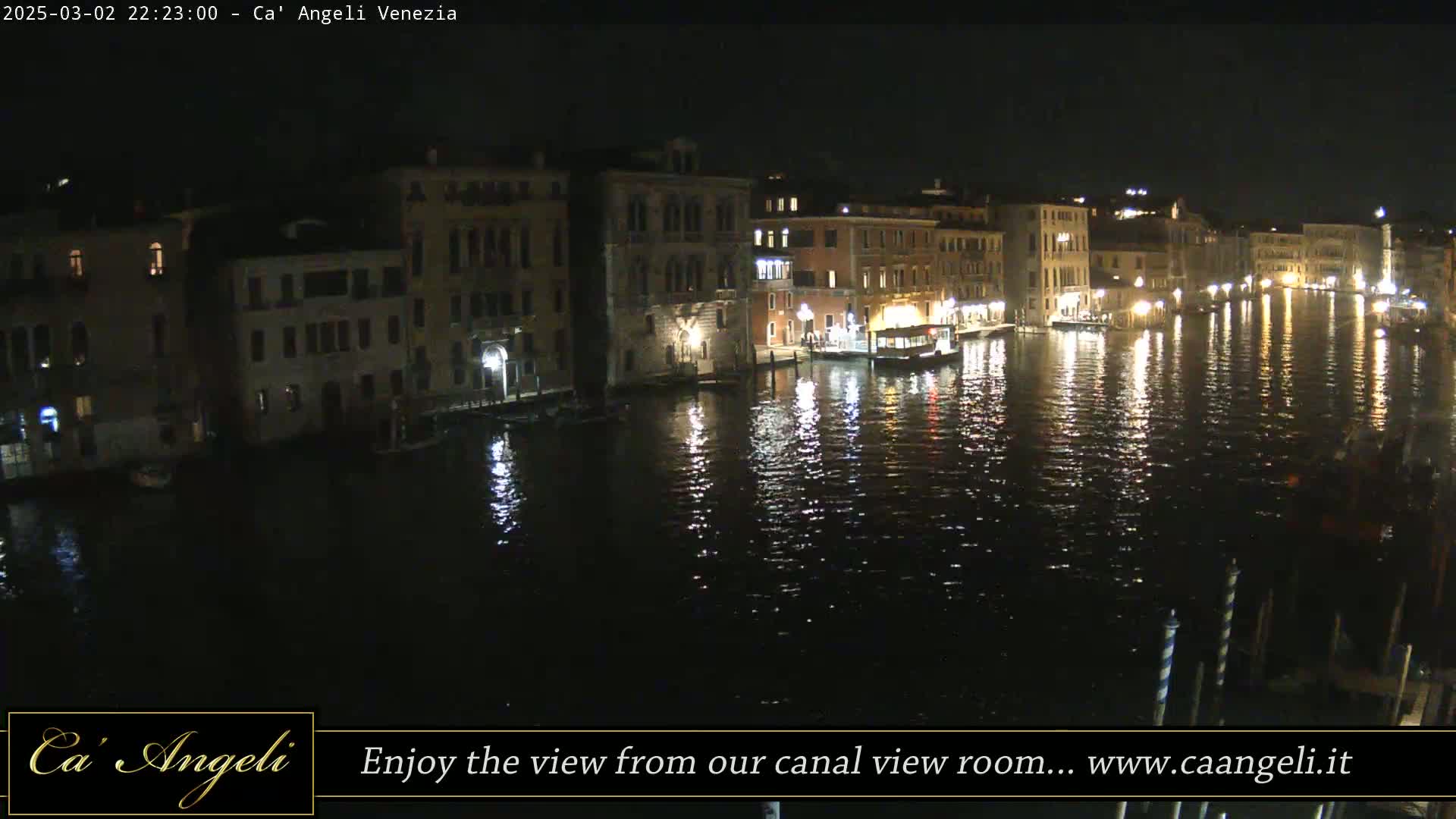 A nighttime view of a canal in Venice, Italy, shows several buildings lit along the waterway, their lights reflecting on the dark water.