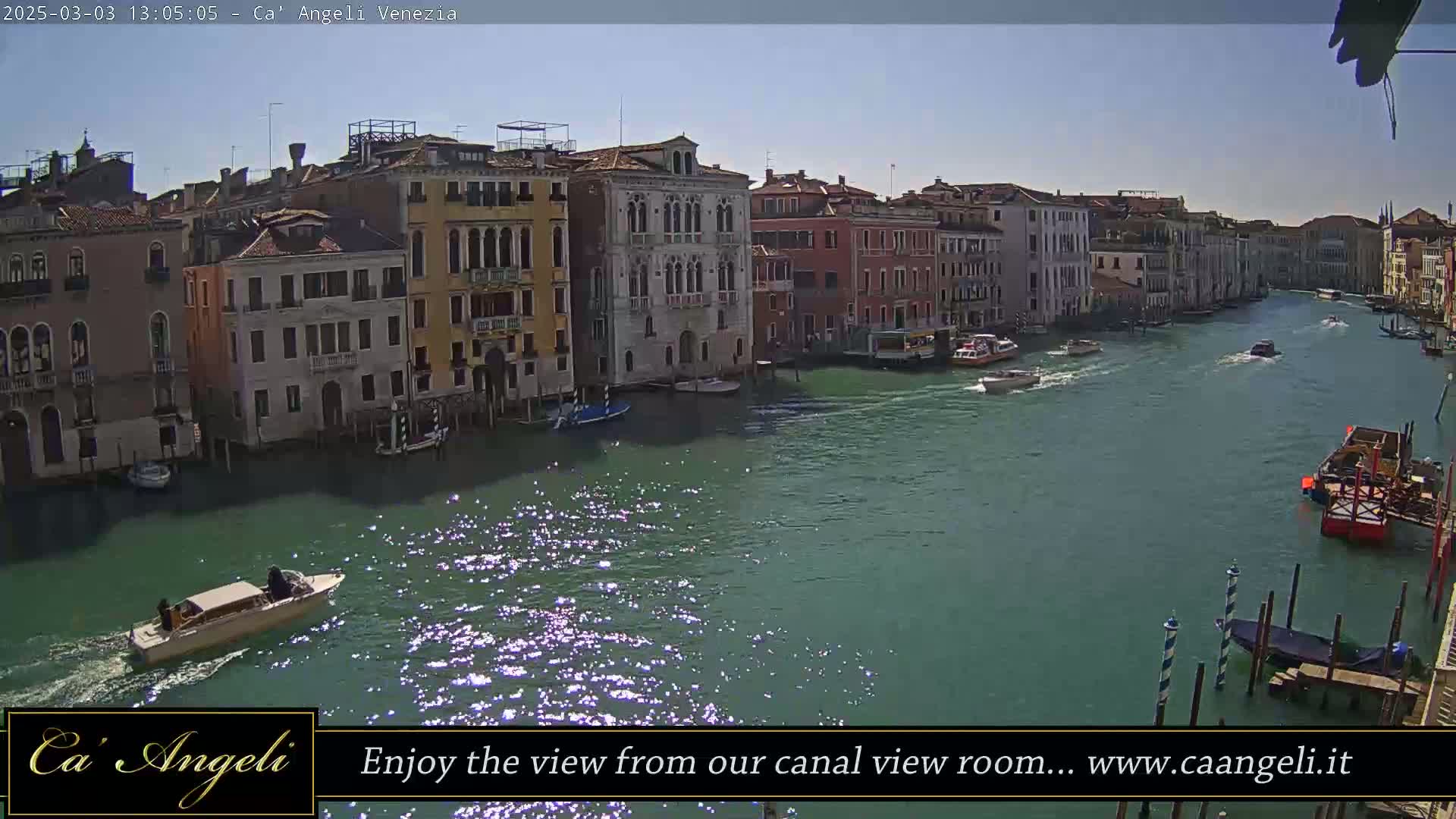 A sunny day in Venice shows a canal lined with buildings, boats traveling on the water, and sunlight glinting off the surface.