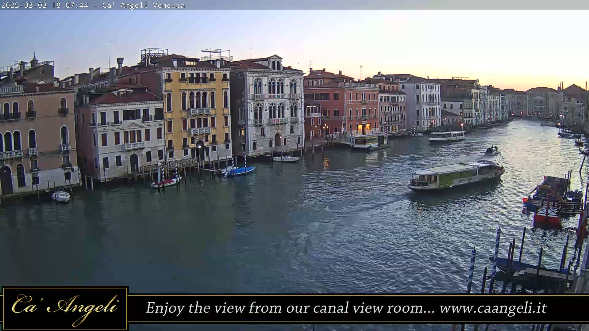 A twilight view of a Venetian canal, showing colorful buildings lining the waterway, with several boats and water taxis navigating the calm waters.