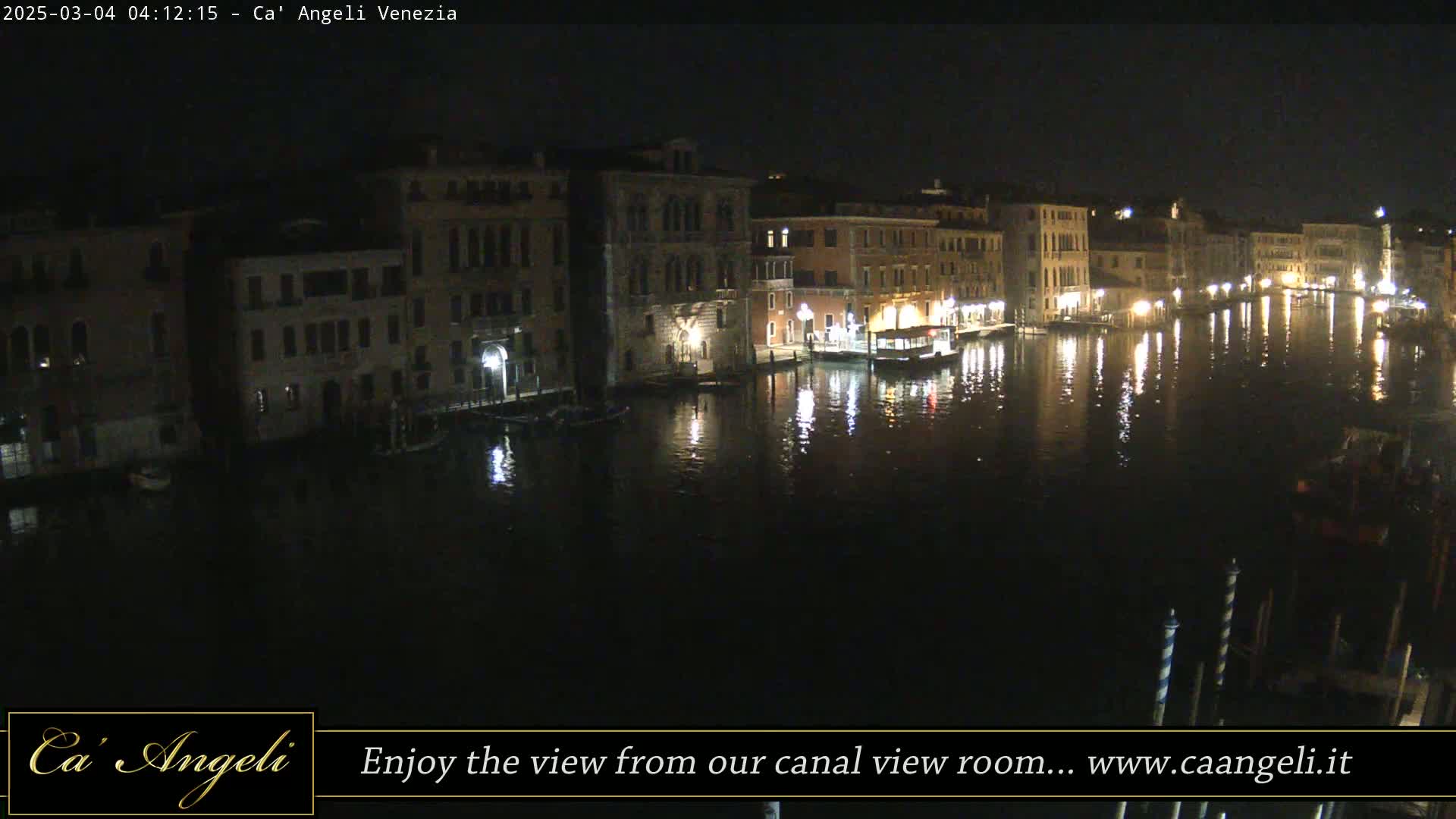 A nighttime view of a canal in Venice, Italy, shows buildings lining the waterway, their lights reflecting on the dark water.