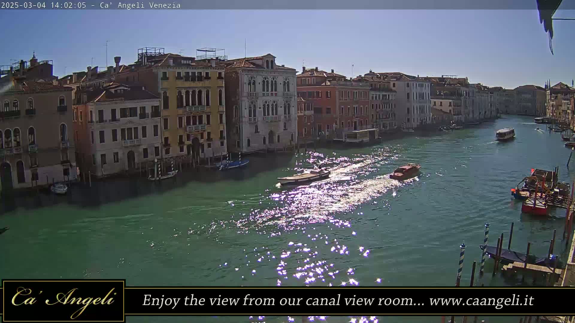 A sunny day in Venice shows several boats on a canal lined with buildings.
