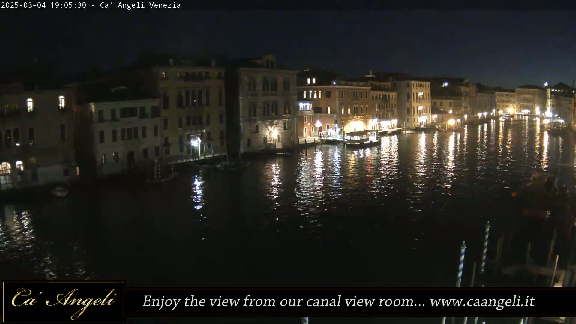 A nighttime view of a canal in Venice, with illuminated buildings lining the waterway and reflections shimmering on the dark water.