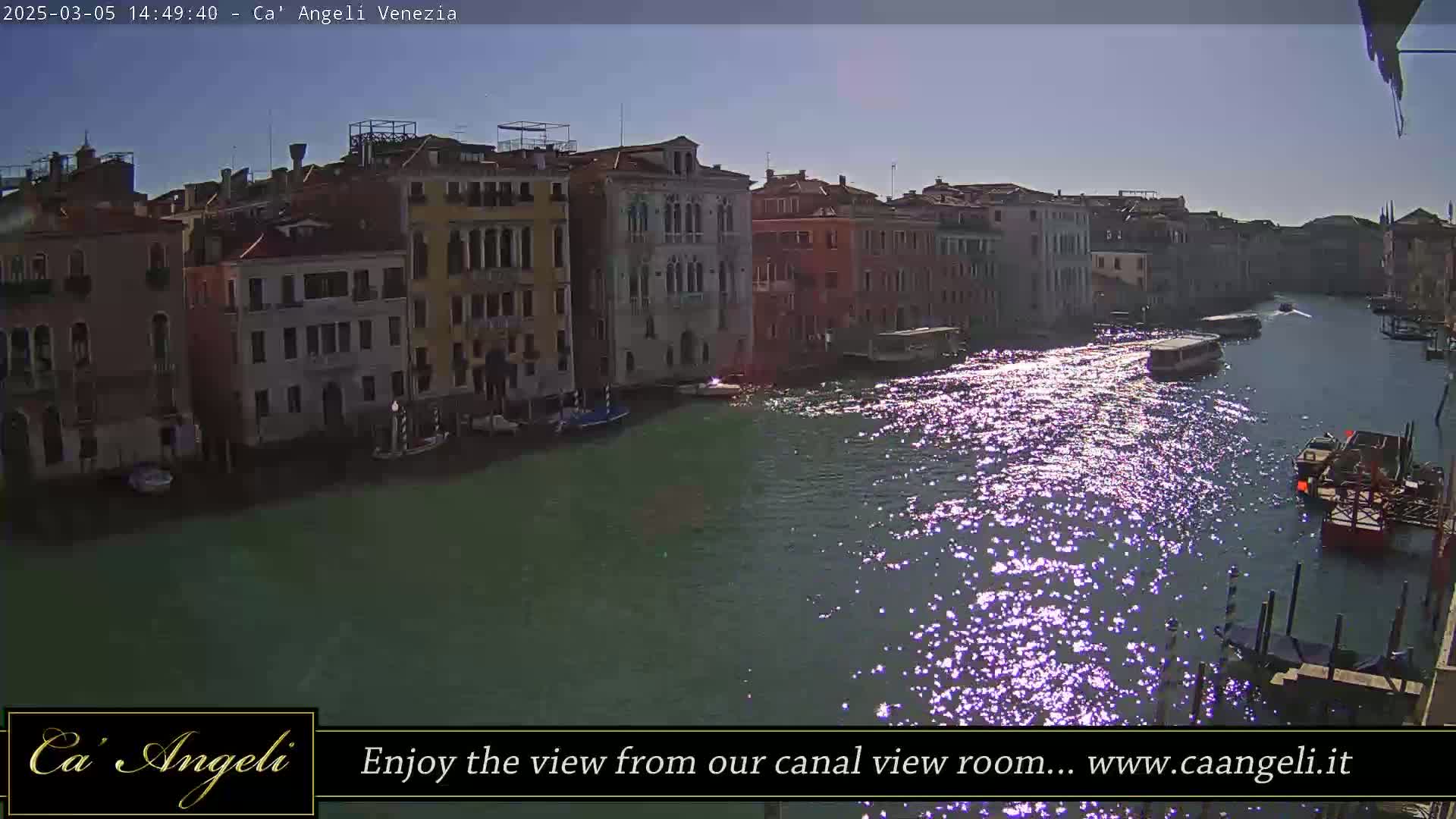 A sunny day shows a Venetian canal reflecting sunlight, with several boats and buildings lining the waterway.
