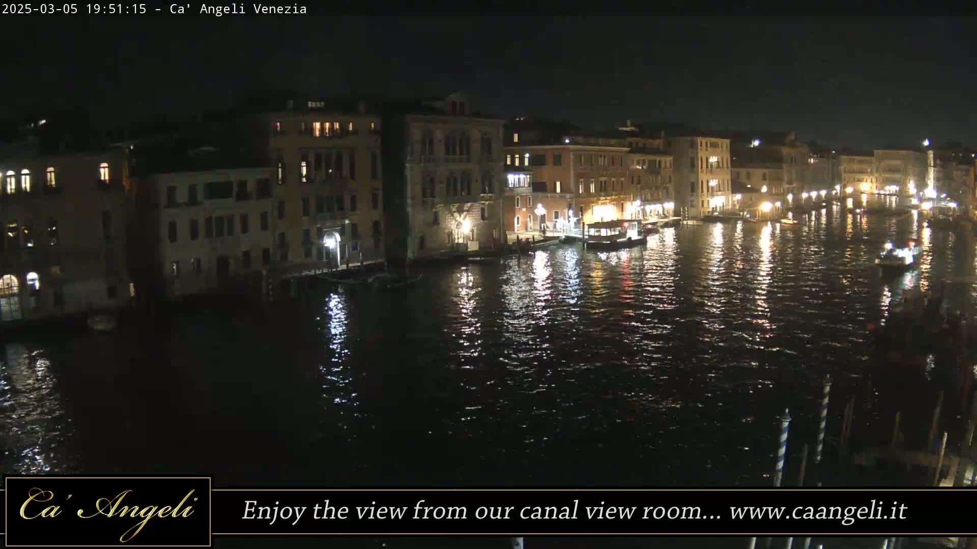A nighttime view of a canal in Venice, Italy, with illuminated buildings lining the waterway and boats moored along the banks.