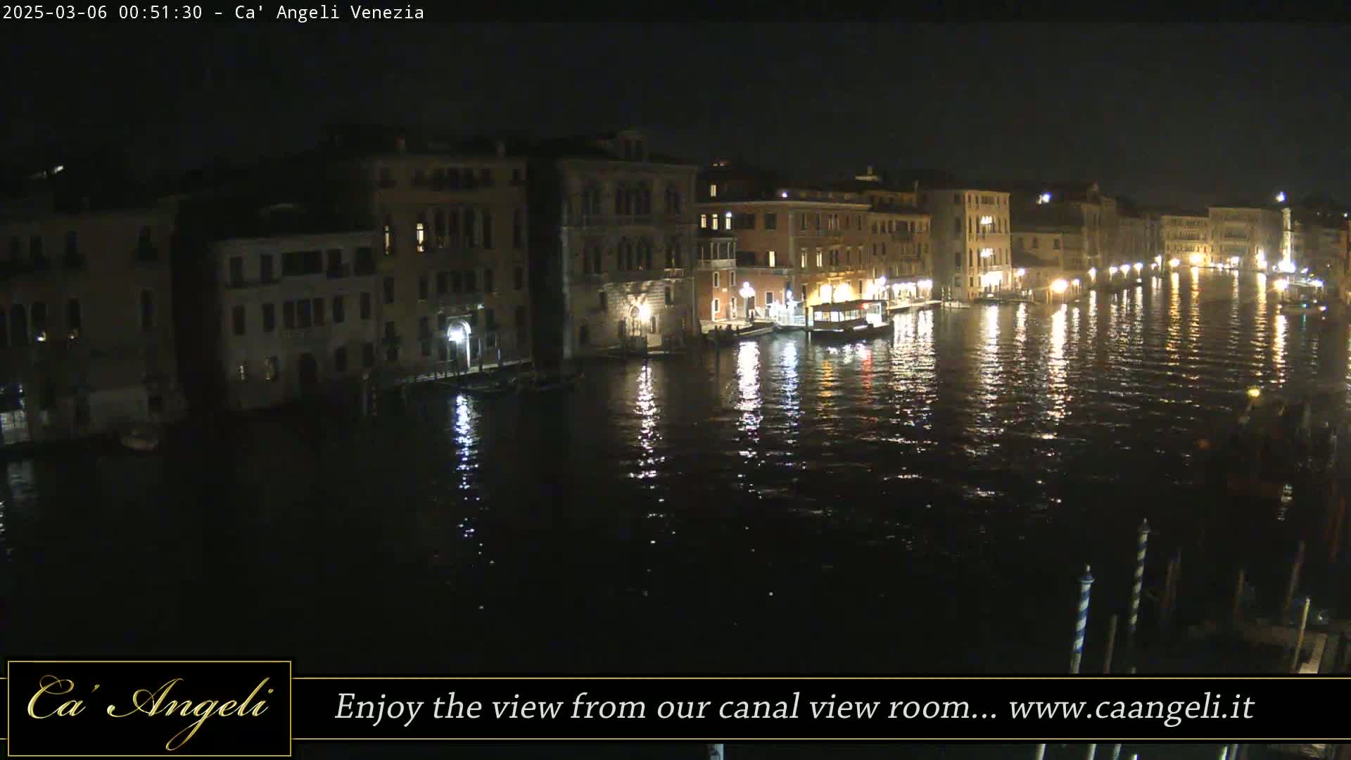 Dark buildings line a calm canal at night, their lights reflecting on the water.