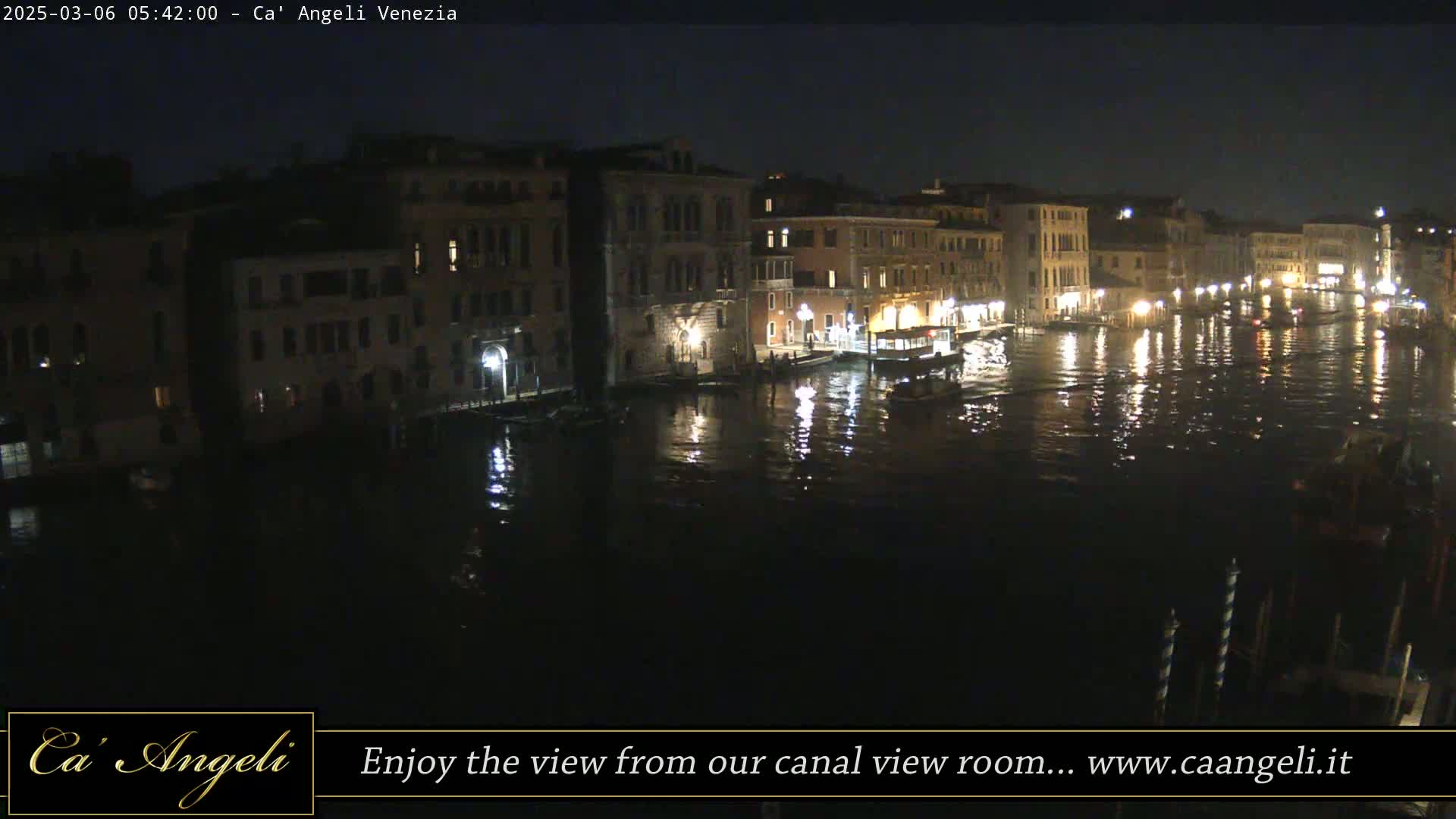 A nighttime view of a canal in Venice, with several buildings illuminated along its banks and boats on the water.