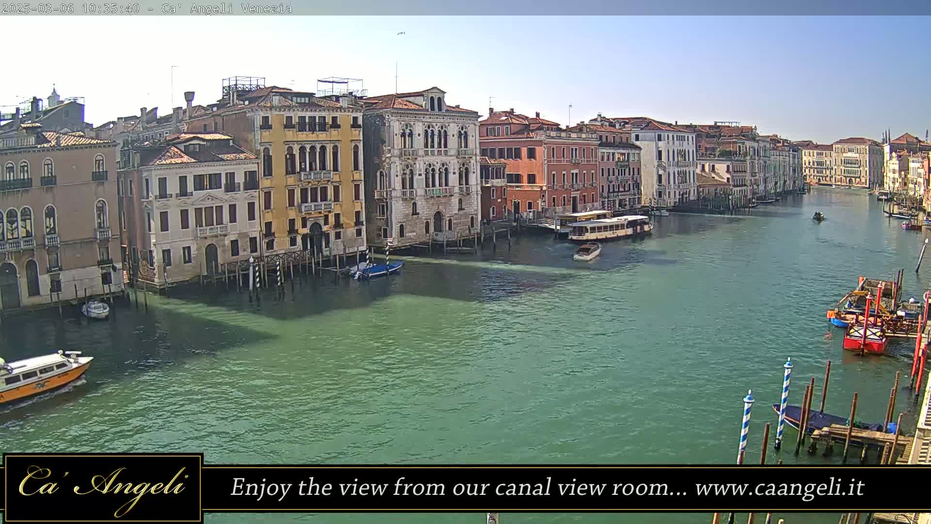 A sunny day in Venice shows a wide canal with several boats and colorful buildings lining the waterway.