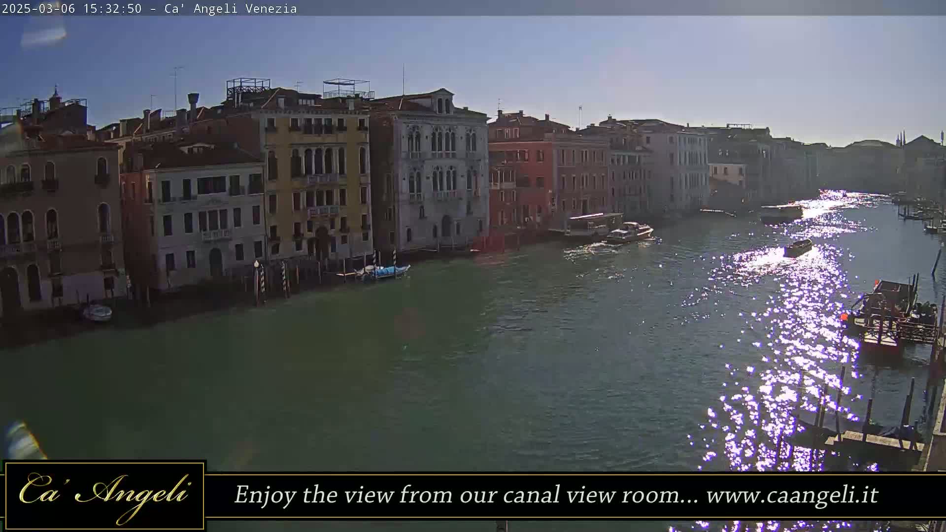 A sunny day in Venice shows a canal with several boats, reflecting sunlight, and buildings lining the waterway.
