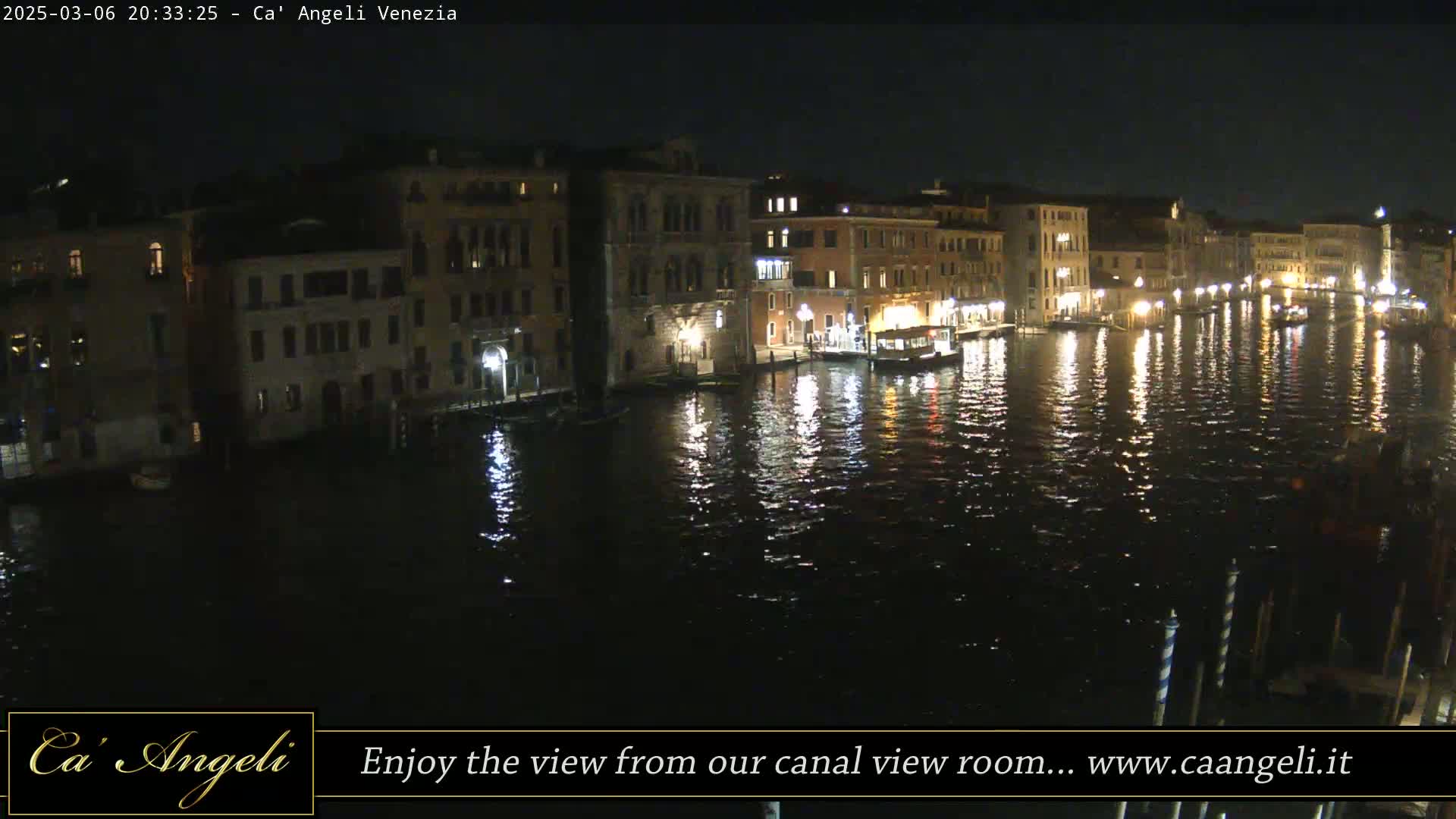 A nighttime view of a canal in Venice, lined with illuminated buildings, reflecting in the dark water.